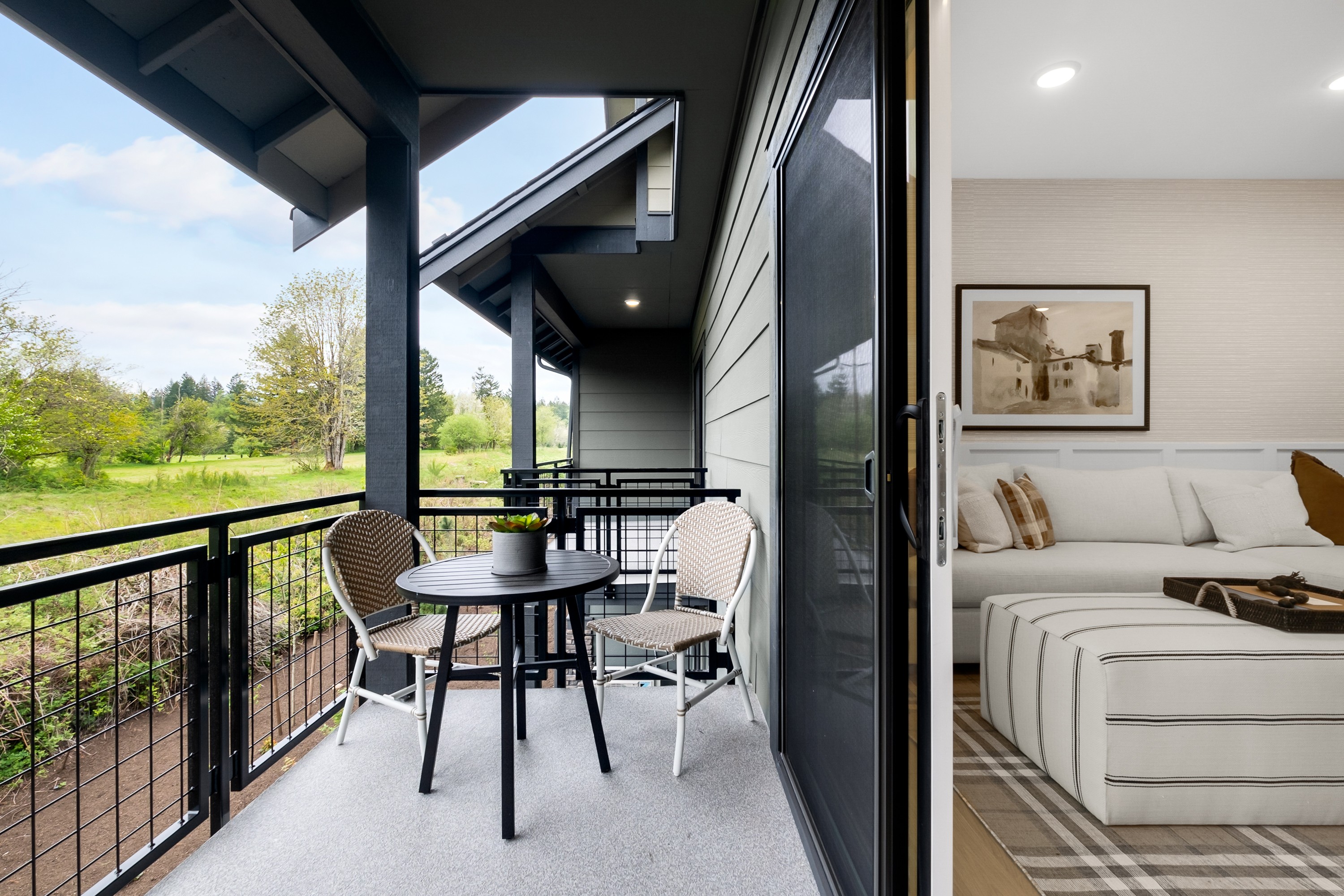 A modern, open-concept living space with a balcony overlooking a lush, green outdoor area.