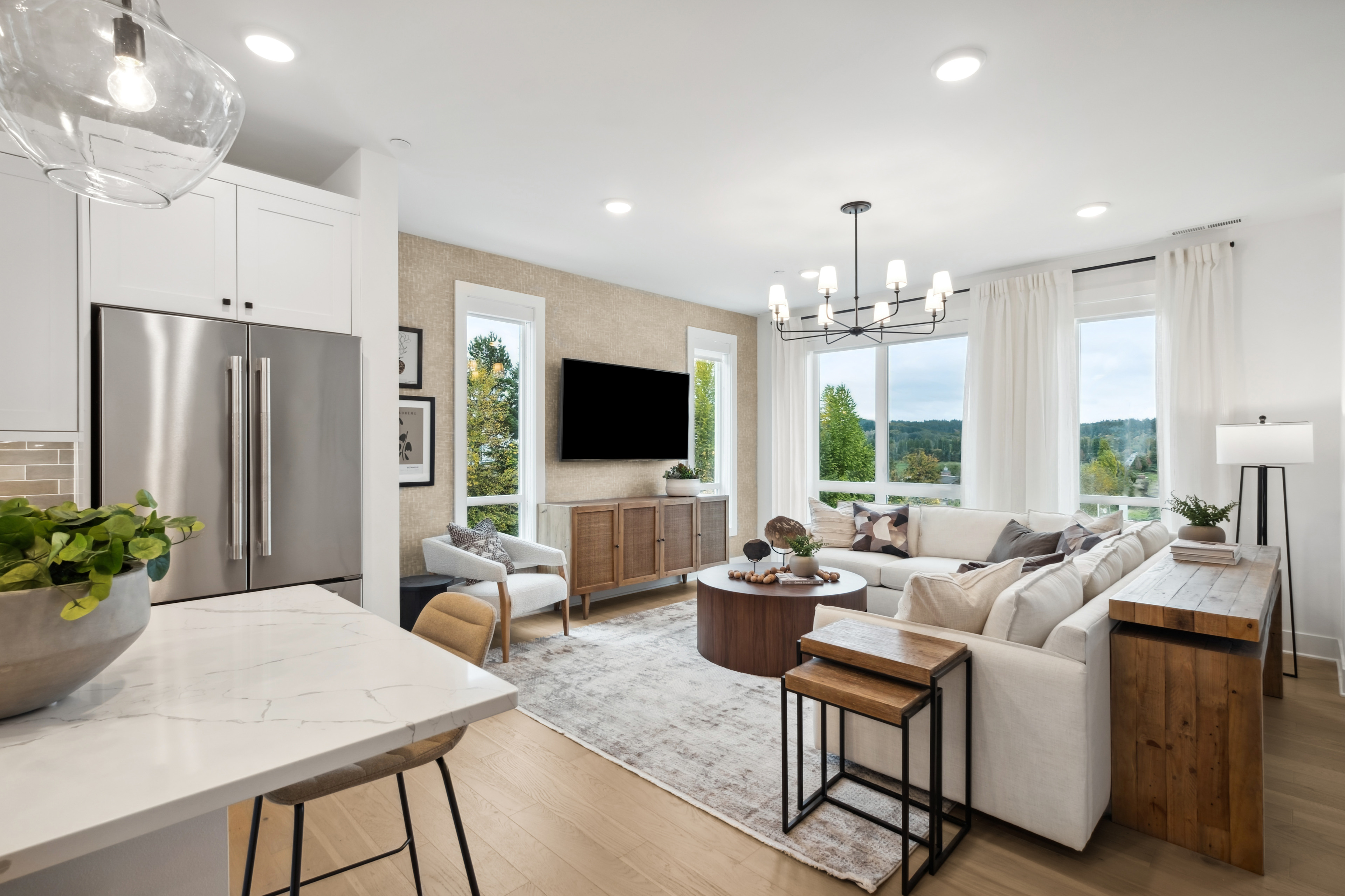 A modern and spacious living room with a kitchen area, featuring a large window overlooking a scenic outdoor view, comfortable seating, and a mix of contemporary and rustic design elements.