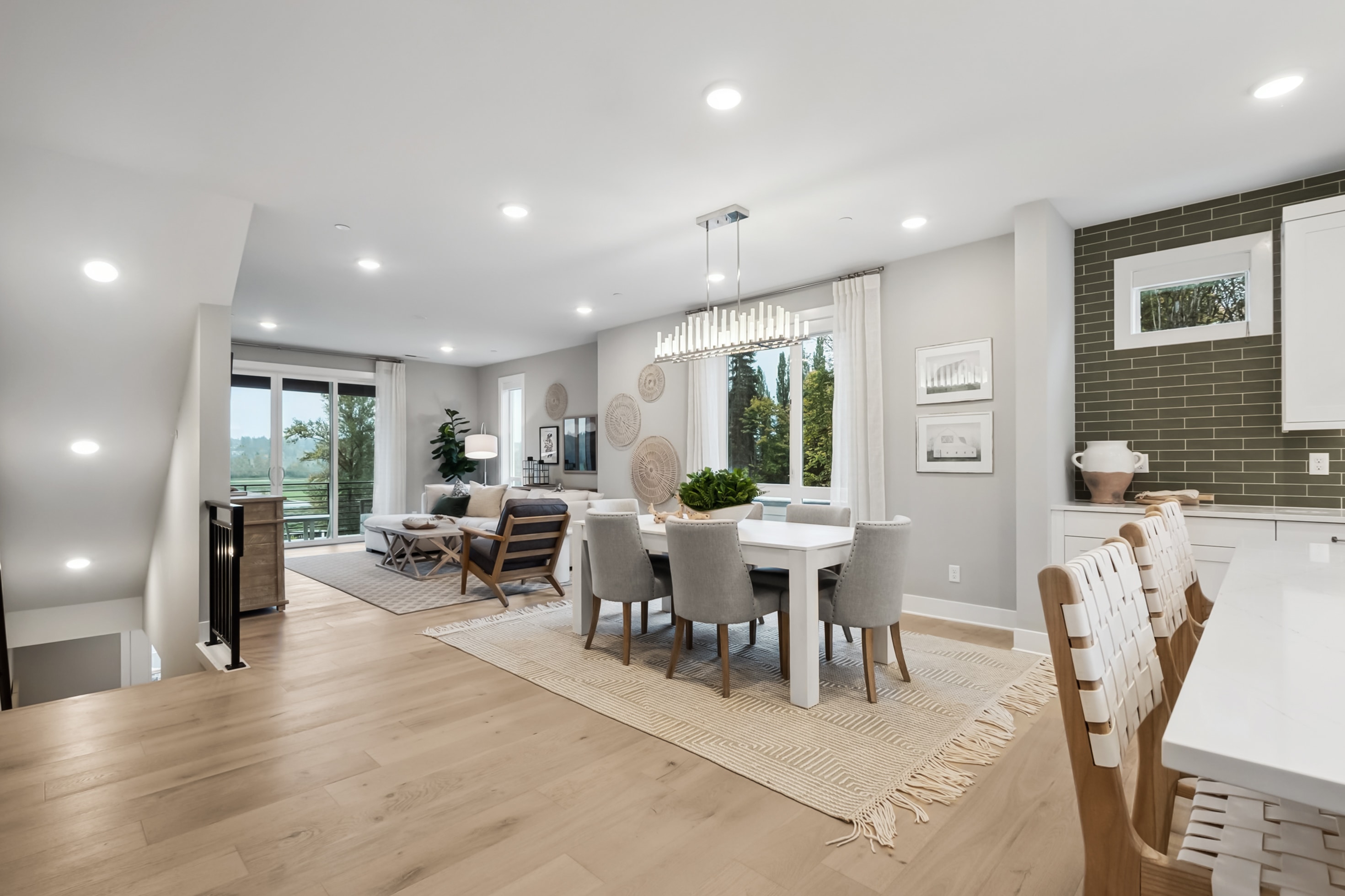 A spacious and well-lit open-concept living and dining area with hardwood floors, white walls, and a mix of modern and rustic furnishings, including a dining table, chairs, and a cozy seating area by the window.