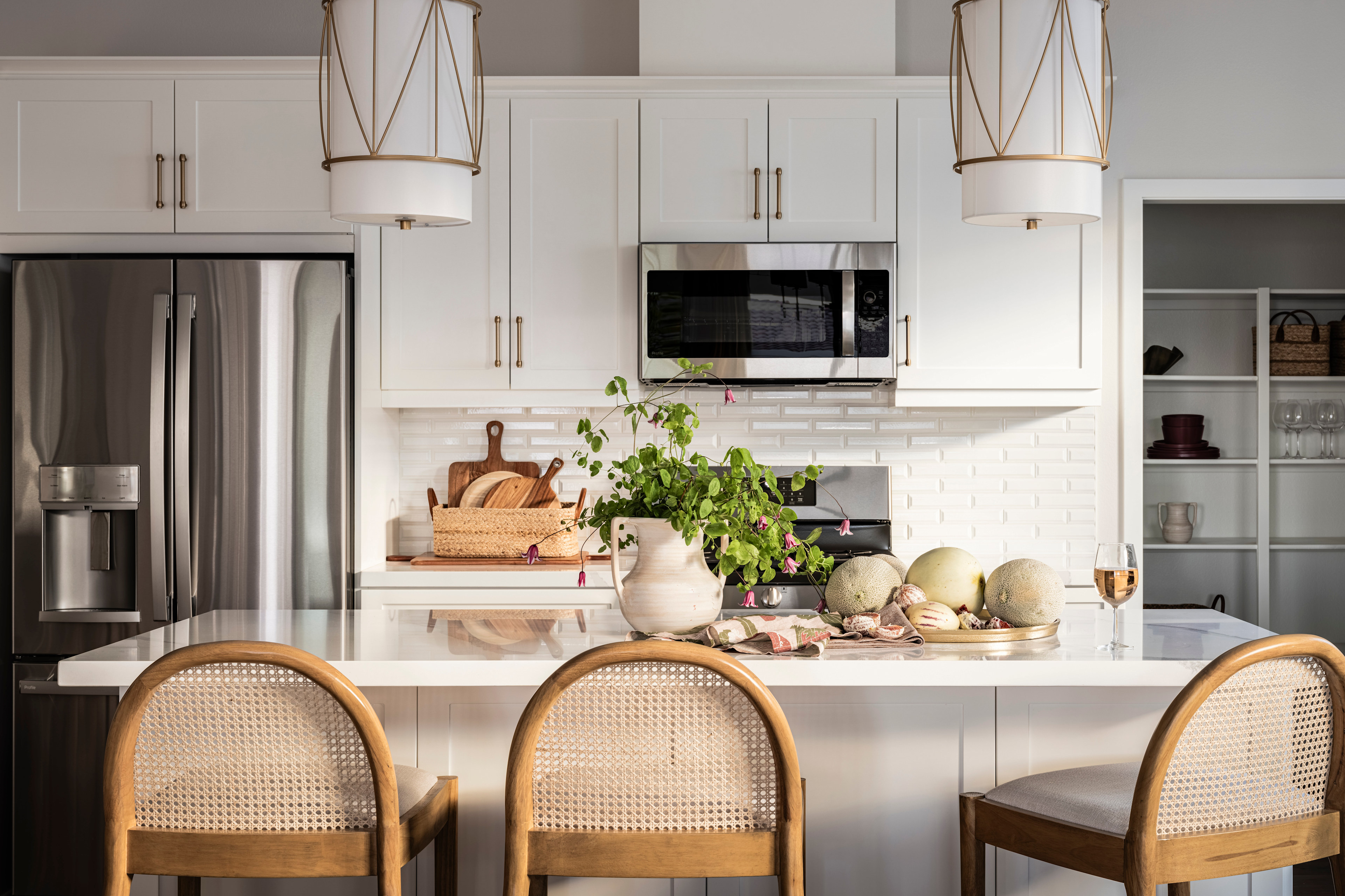 A modern, well-appointed kitchen with white cabinets, stainless steel appliances, and a central island with stools, featuring decorative elements such as plants and pottery.