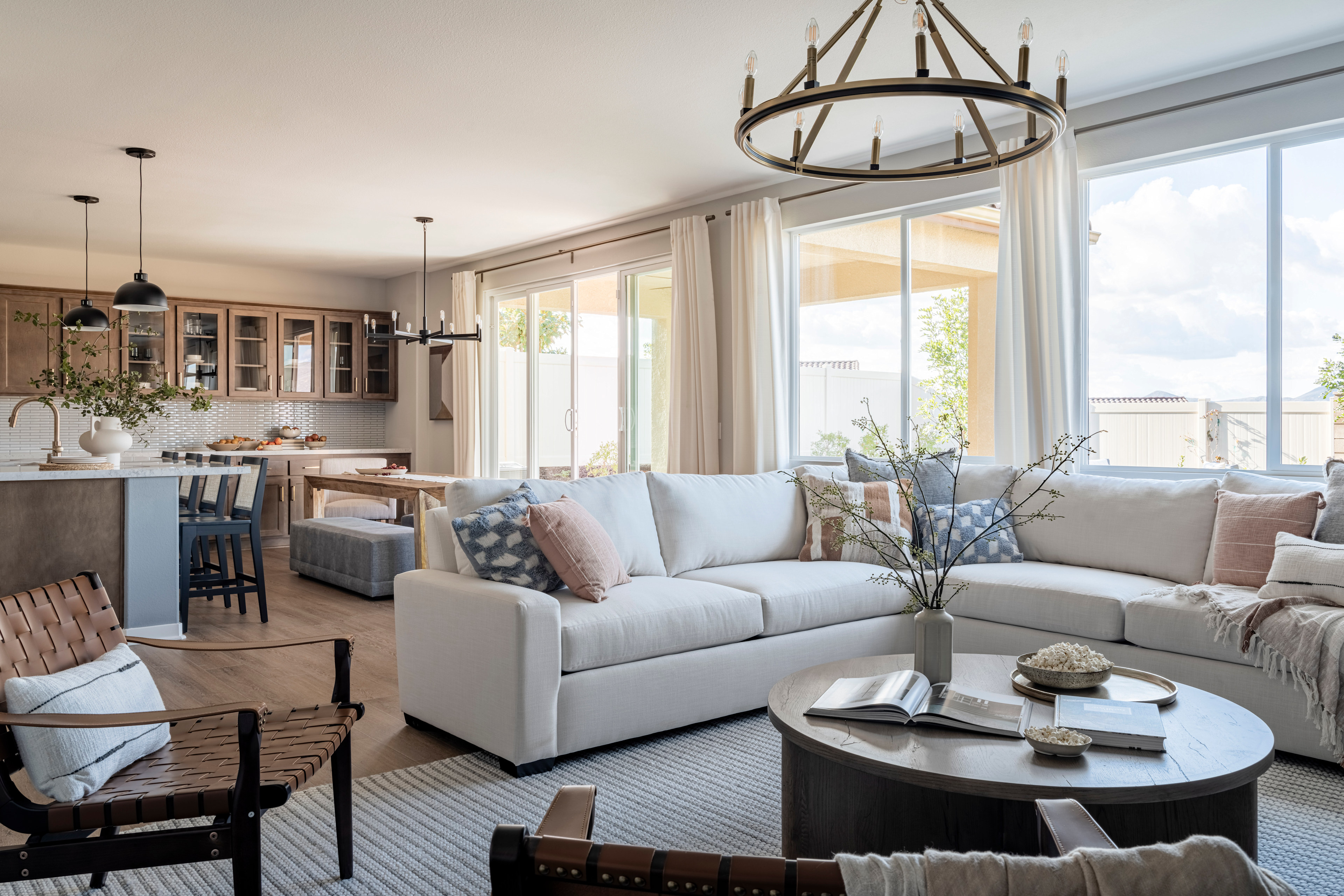 A cozy and inviting living room with a plush sectional sofa, a round coffee table, and a chandelier overhead, surrounded by large windows that let in natural light and offer a view of the outdoor scenery.