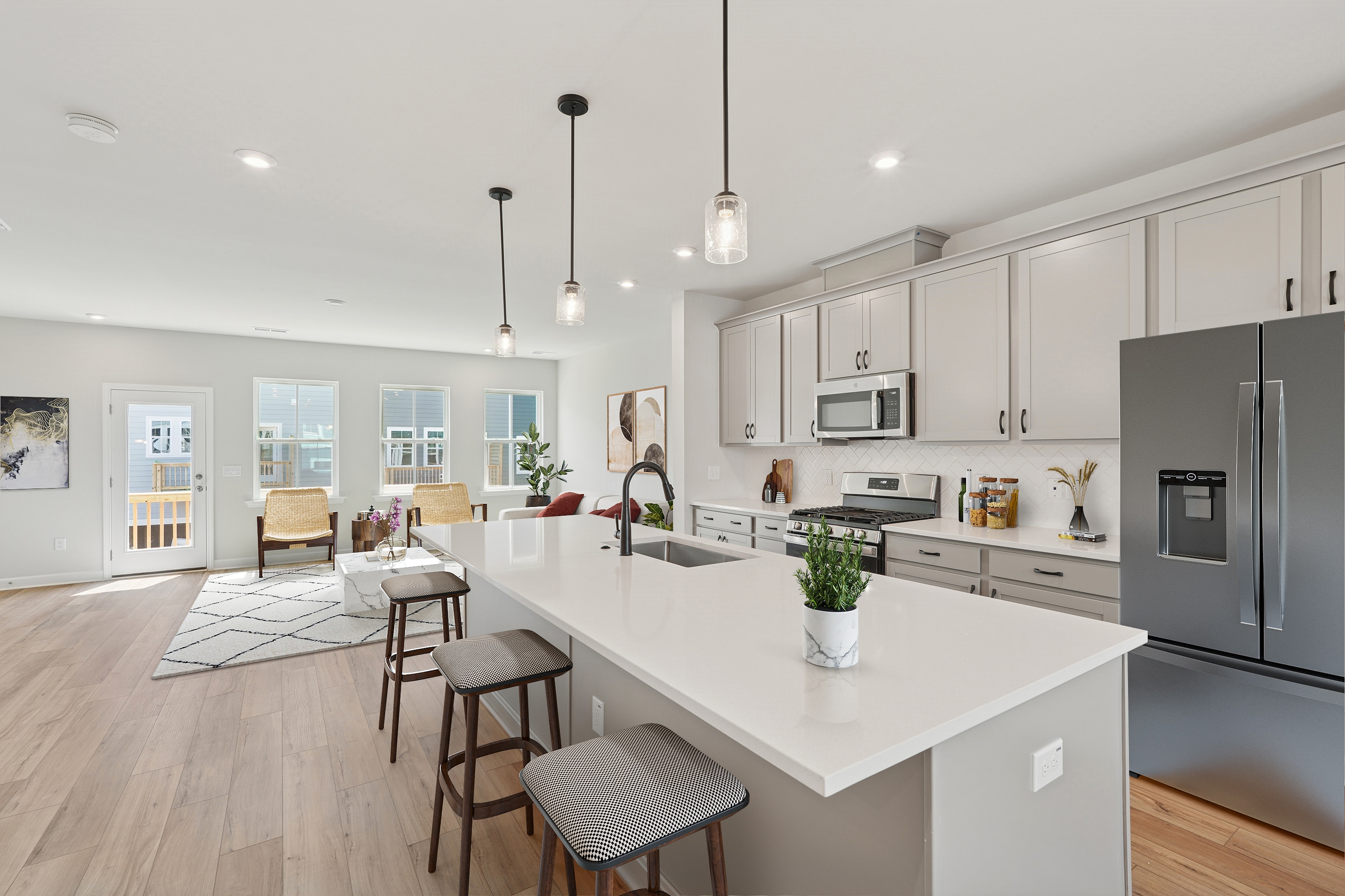 A modern, open-concept kitchen with white cabinets, a large island, and pendant lighting, leading into a living room area with hardwood floors and a cozy seating arrangement.