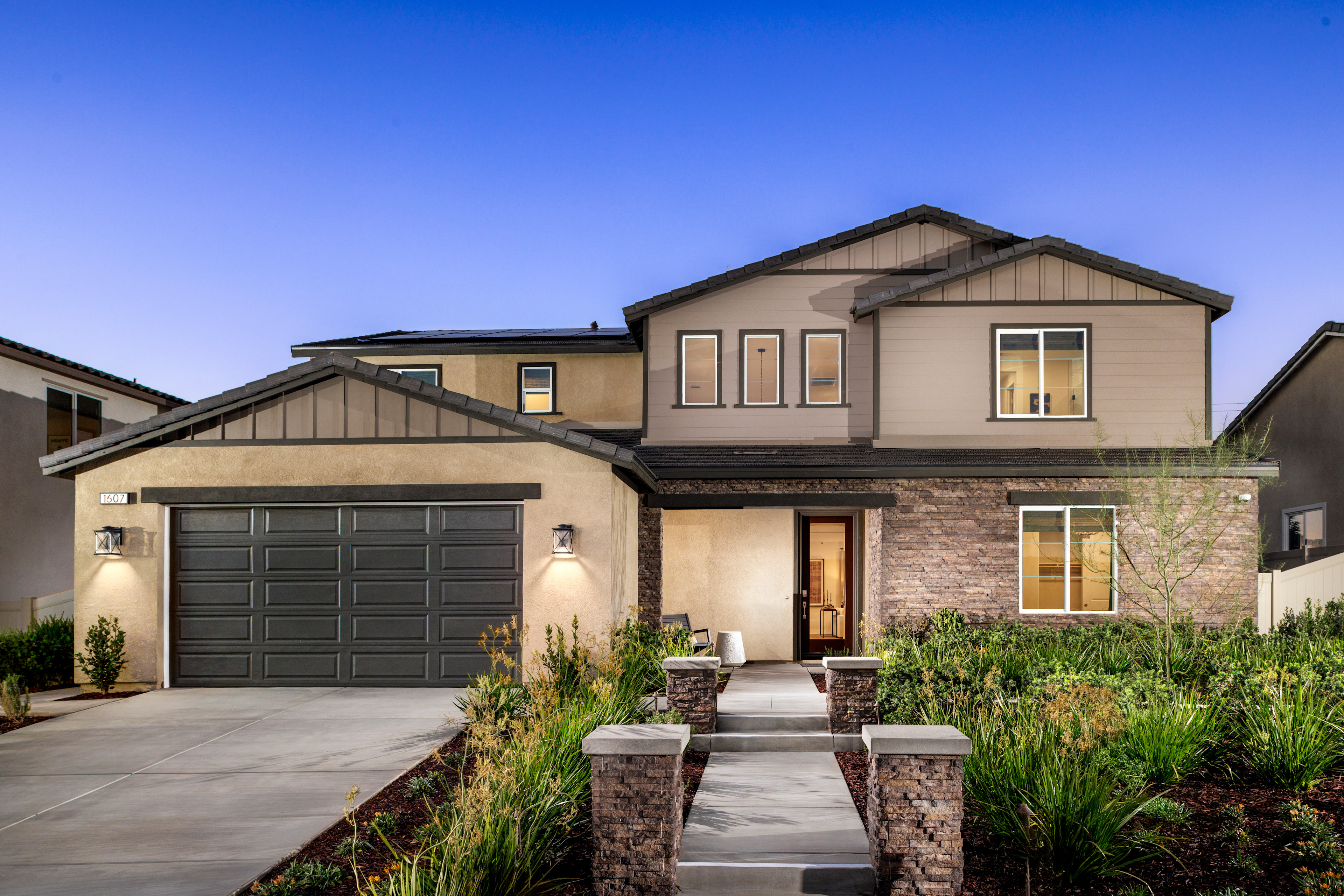 A two-story house with a garage, surrounded by a well-maintained landscaped yard and a clear blue sky in the background.