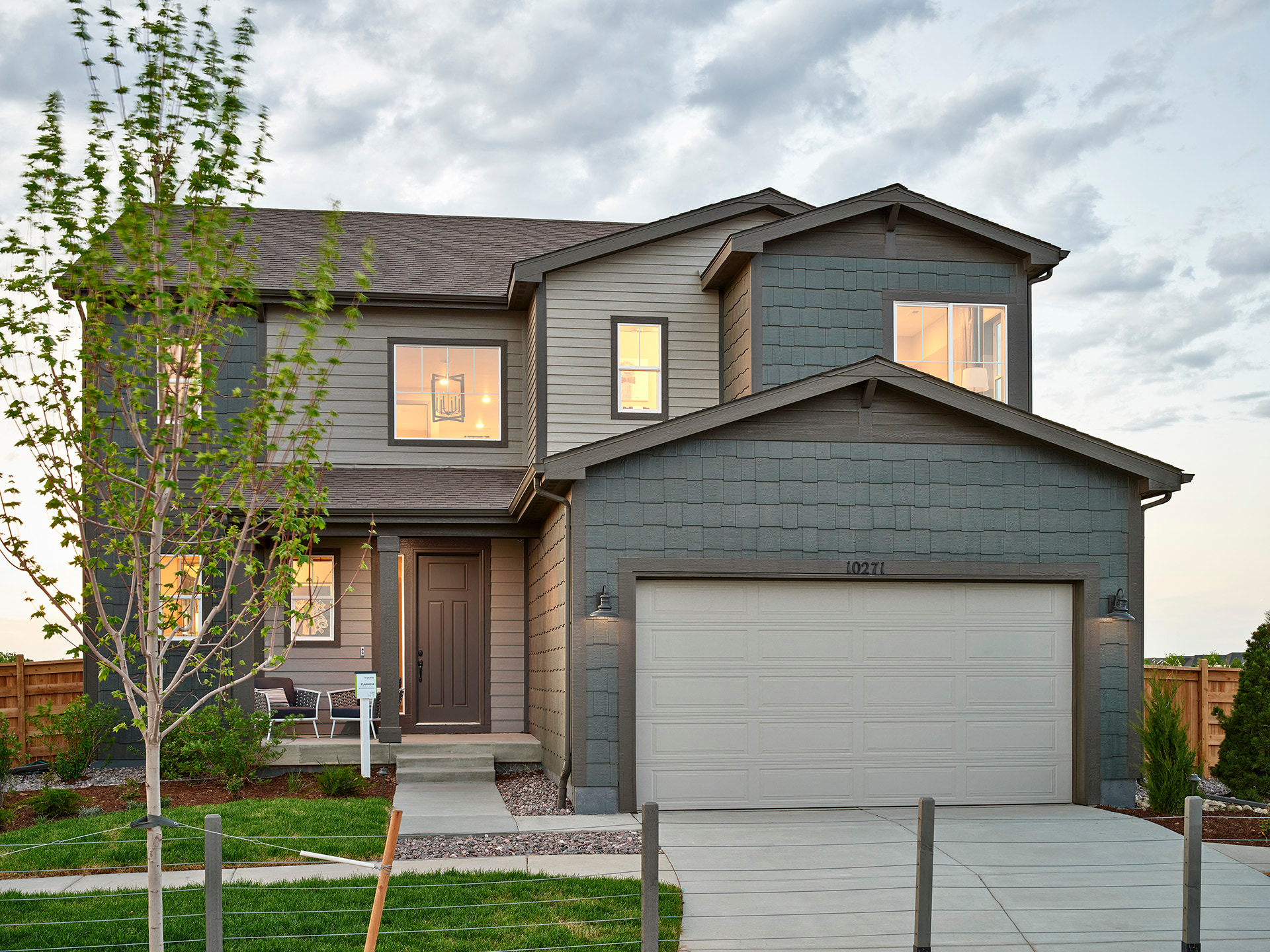 A two-story residential house with a garage, surrounded by a grassy yard and trees in the background.