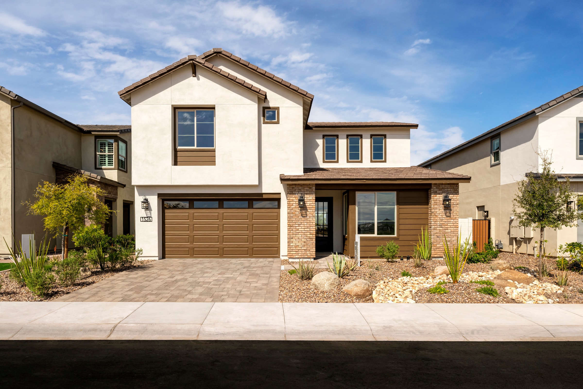 A two-story residential house with a garage, surrounded by landscaped gardens and a clear blue sky in the background.