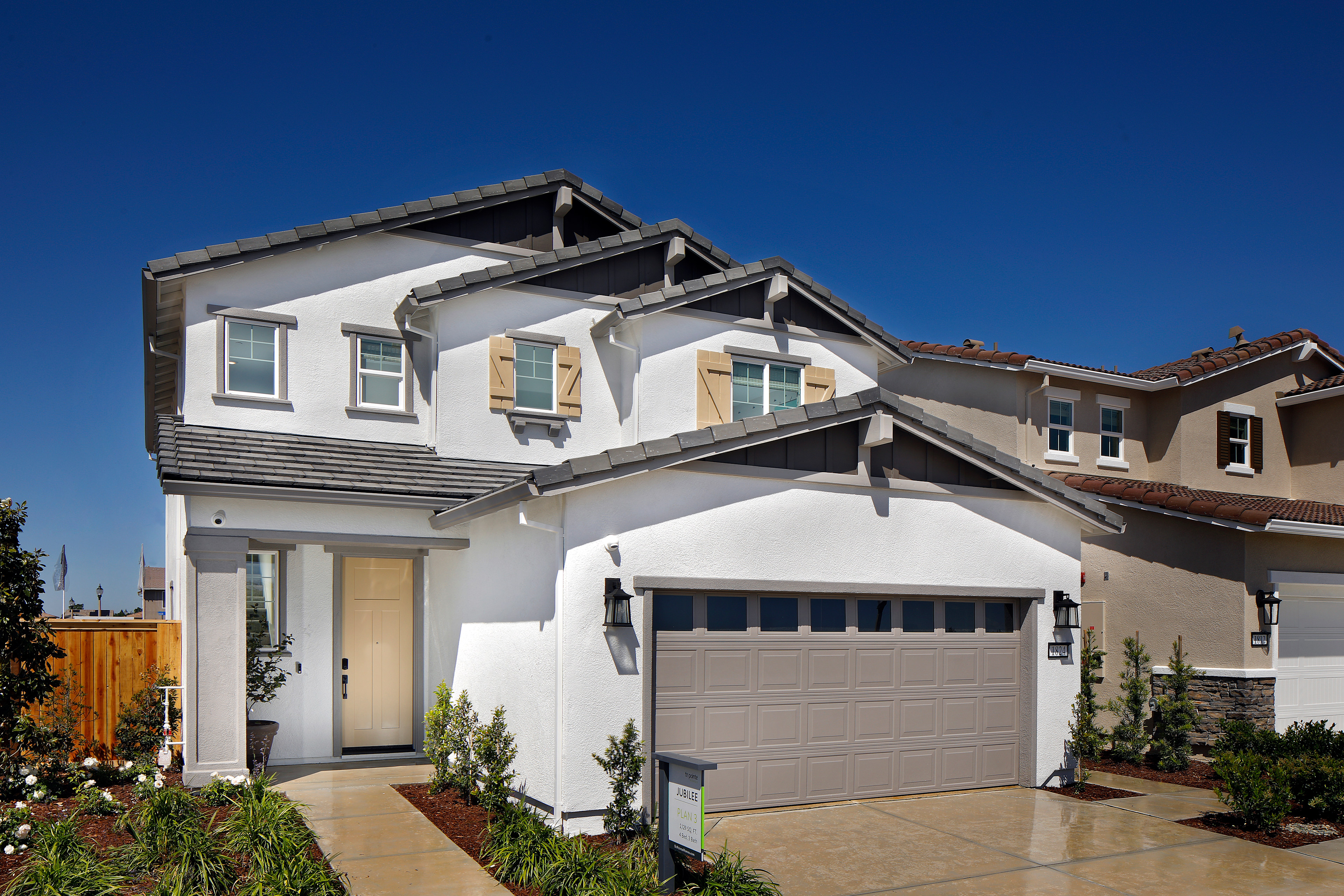 A two-story residential house with a garage, surrounded by a well-maintained lawn and landscaping, set against a clear blue sky.