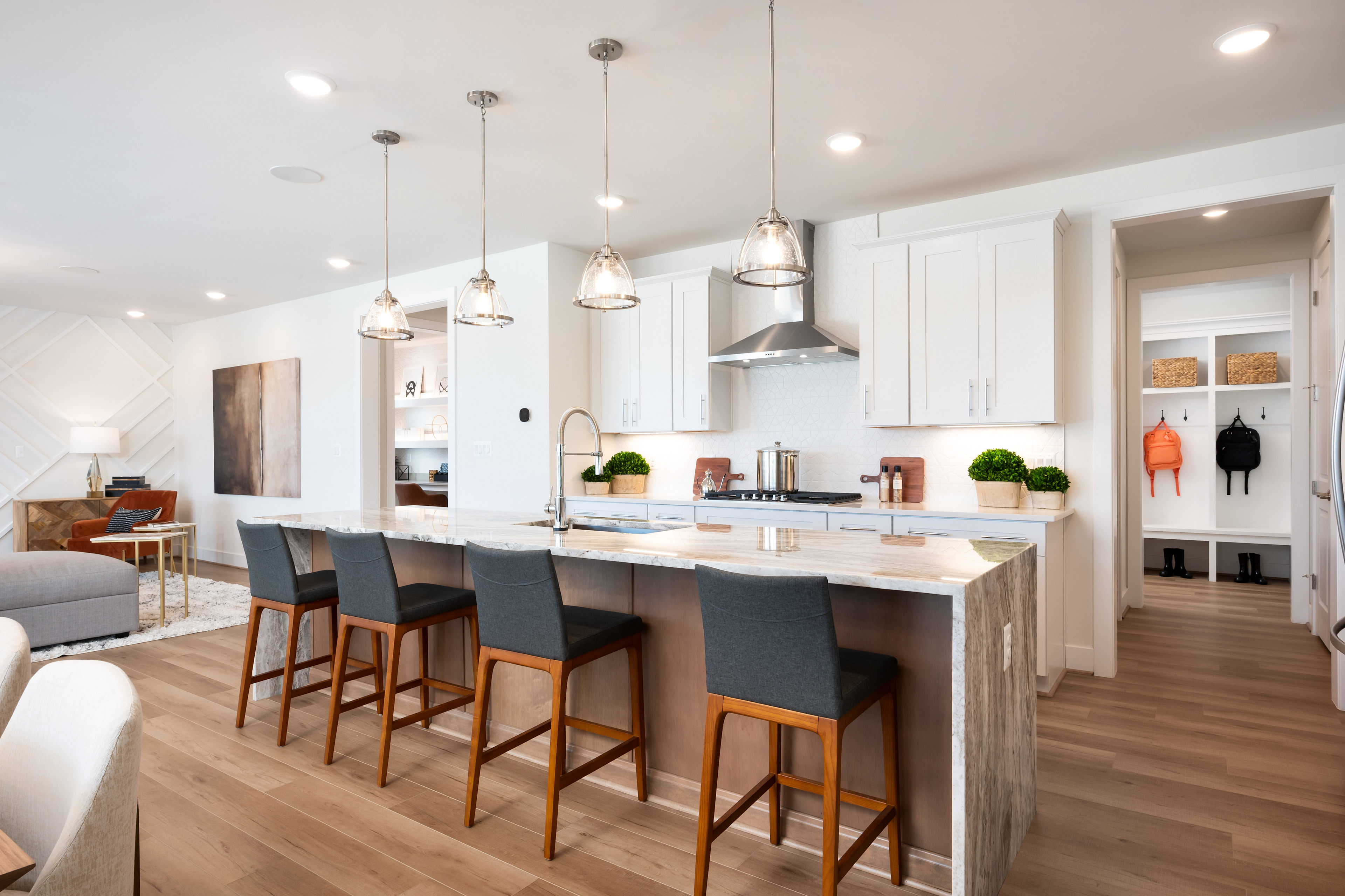 A modern, open-concept kitchen with white cabinets, wooden countertops, and pendant lights hanging above a central island with bar stools.