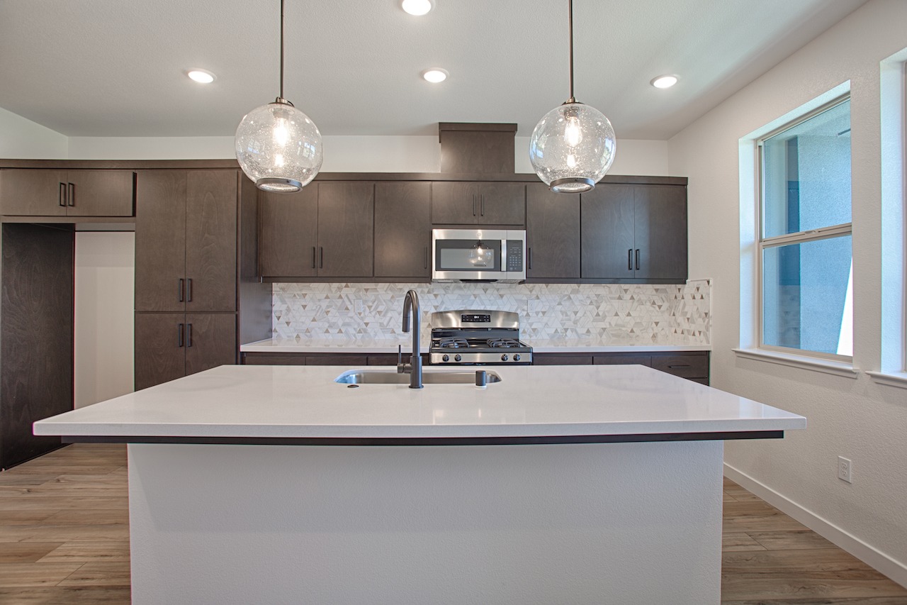 A modern kitchen with dark cabinets, a white countertop, and pendant lights hanging above the island.