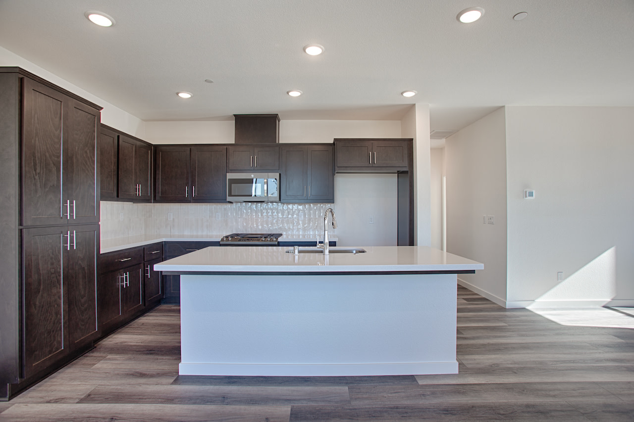 A modern kitchen with dark wood cabinets, a white island, and a tiled backsplash, set against a bright and airy background.