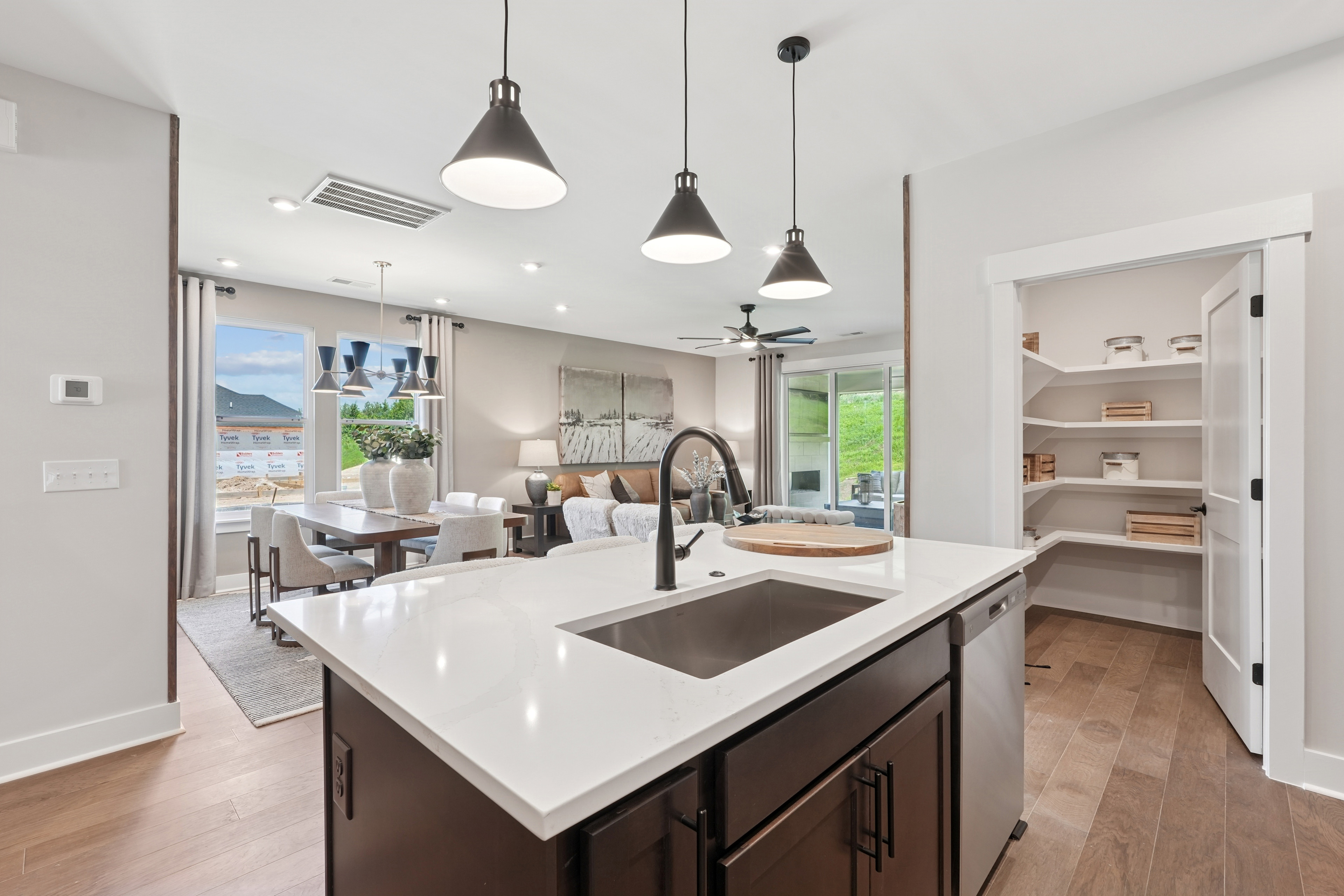 A modern, open-concept kitchen with a large island, white countertops, and pendant lighting fixtures, leading into a dining area with a view of the outdoors.