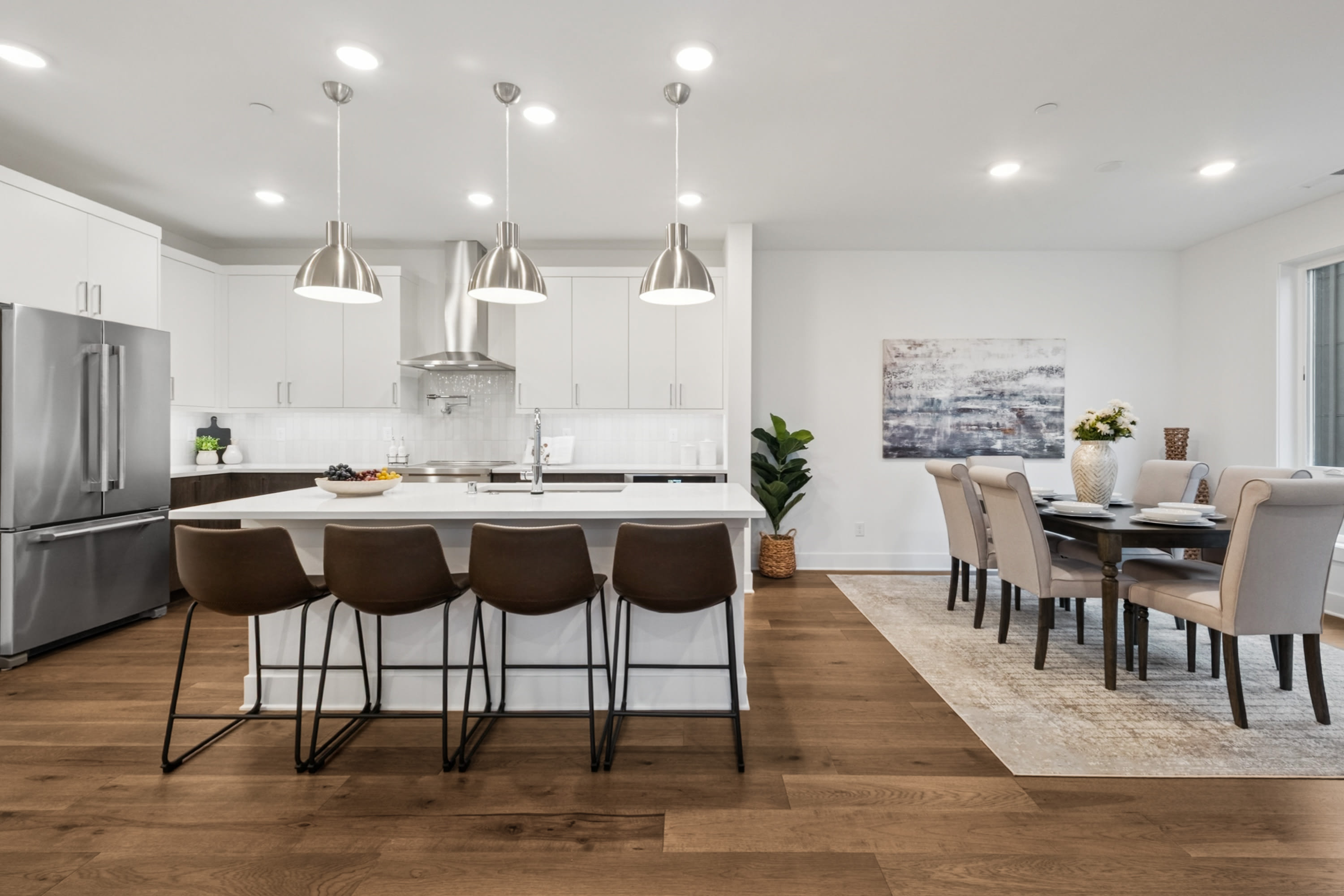 A modern, open-concept kitchen and dining area with a large island, pendant lighting, and a mix of wood and white tones throughout the space.