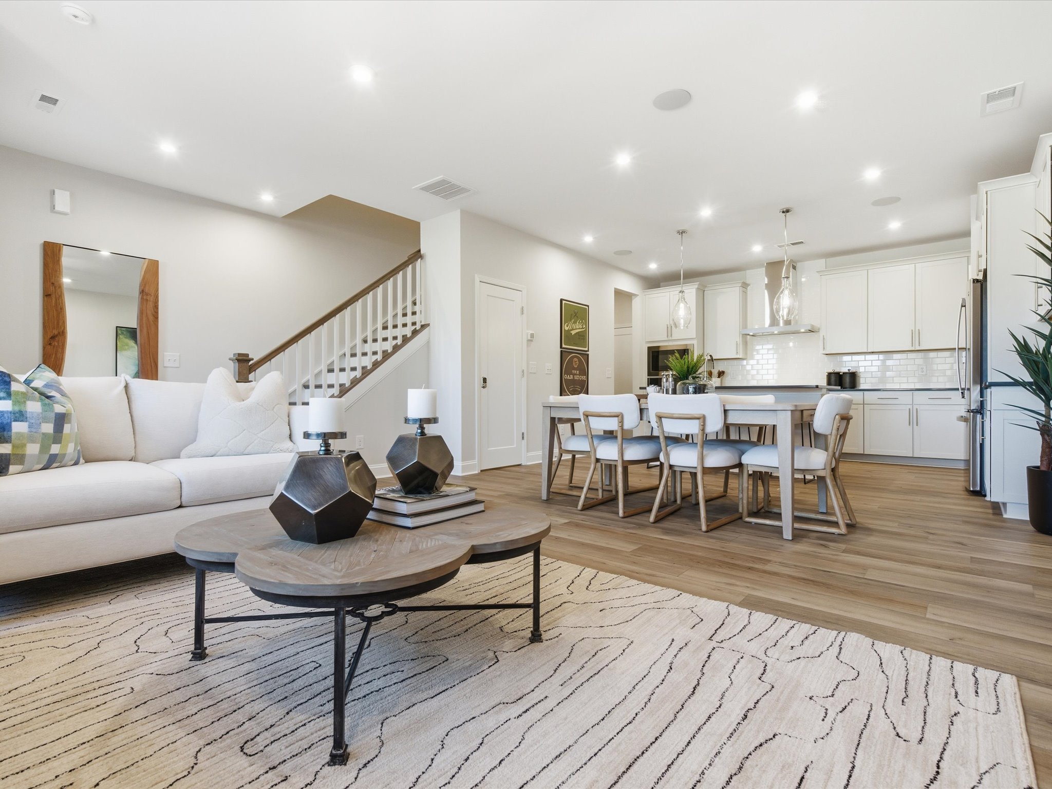 A modern and spacious open-concept living room and kitchen area with a wooden floor, a round coffee table, and a dining table with chairs.