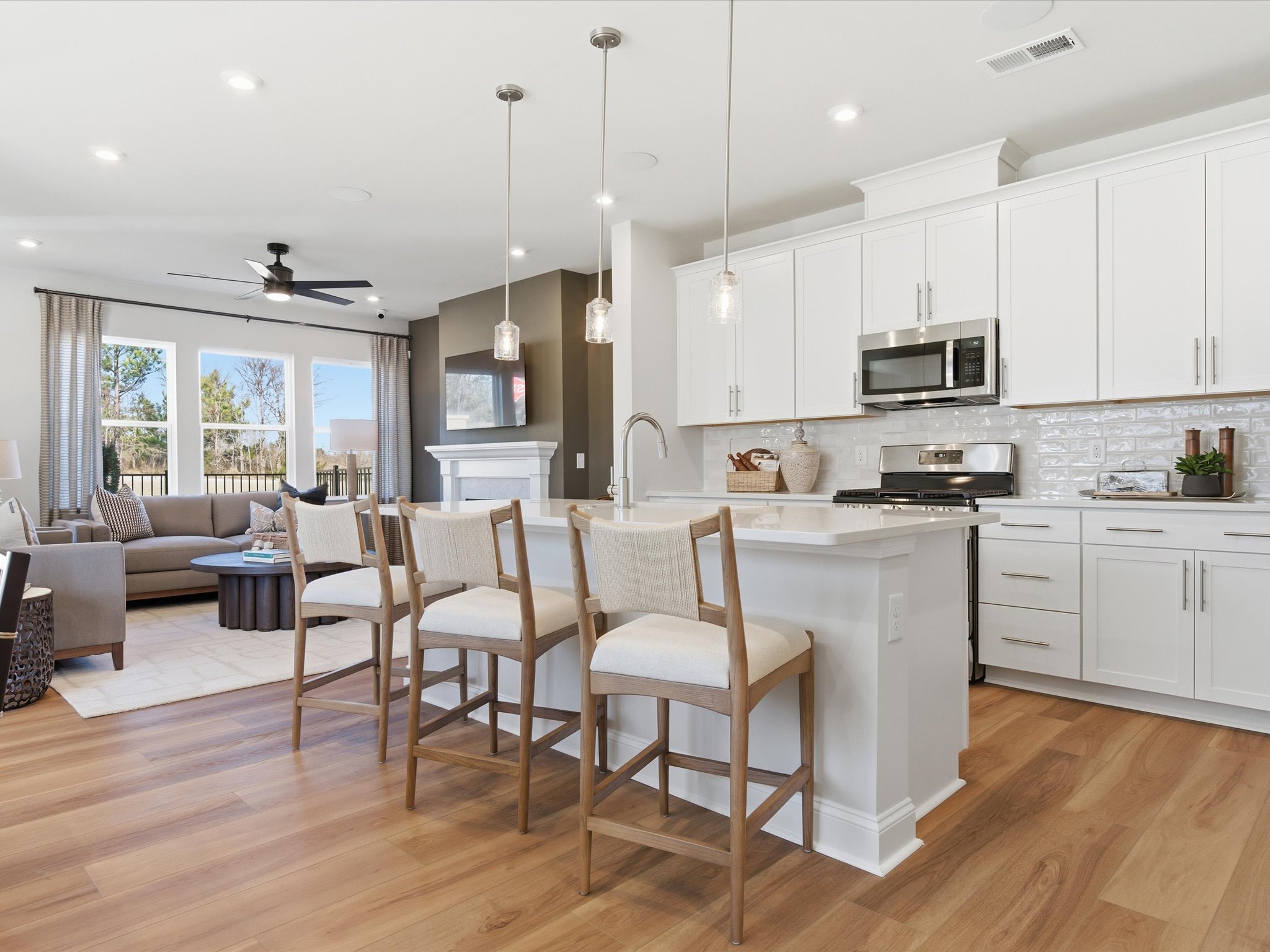 A modern, open-concept kitchen and living room with white cabinets, stainless steel appliances, and hardwood floors, complemented by a cozy seating area and pendant lighting.