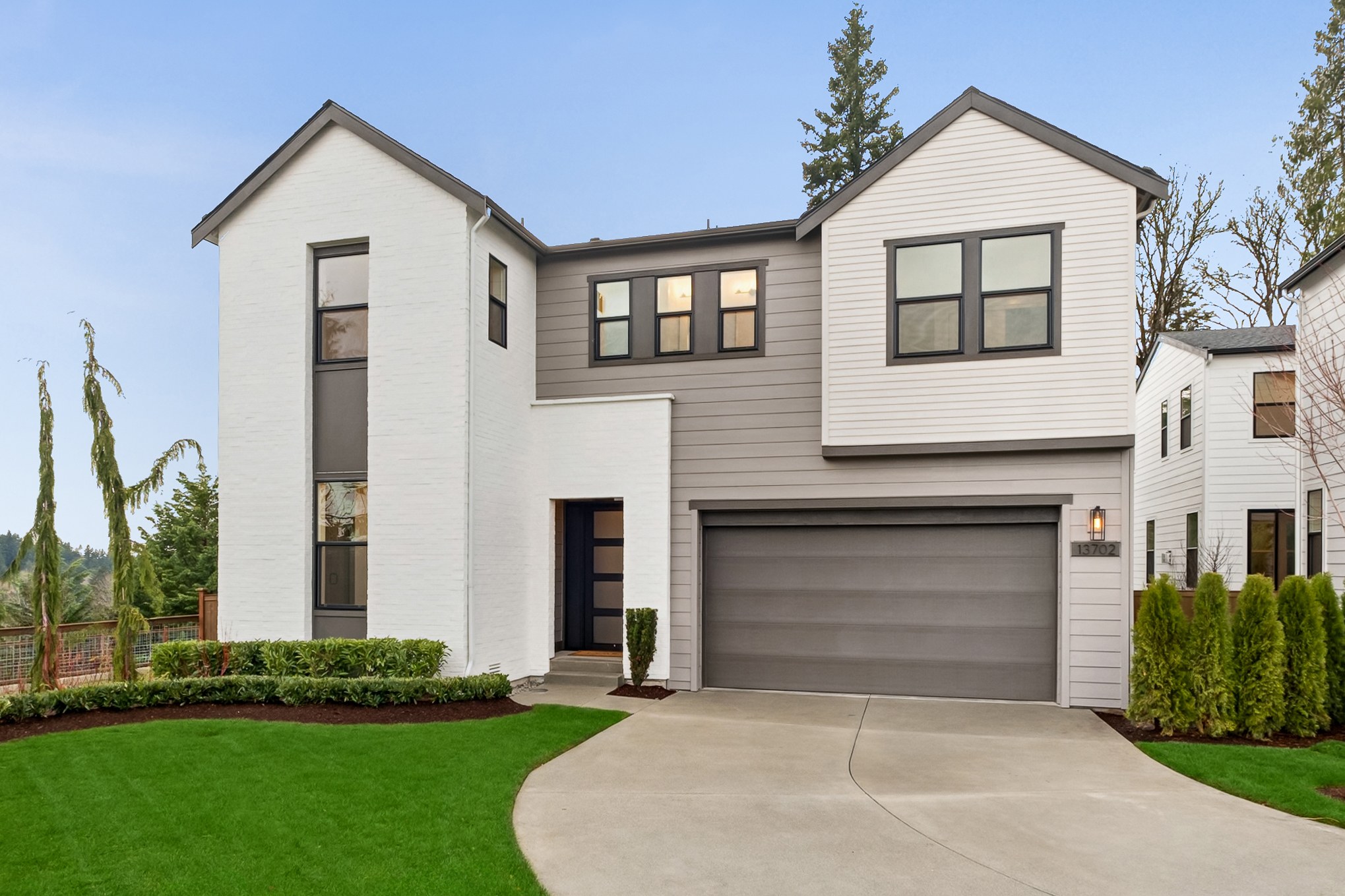 A modern two-story house with a garage, surrounded by a well-manicured lawn and lush greenery in the background.