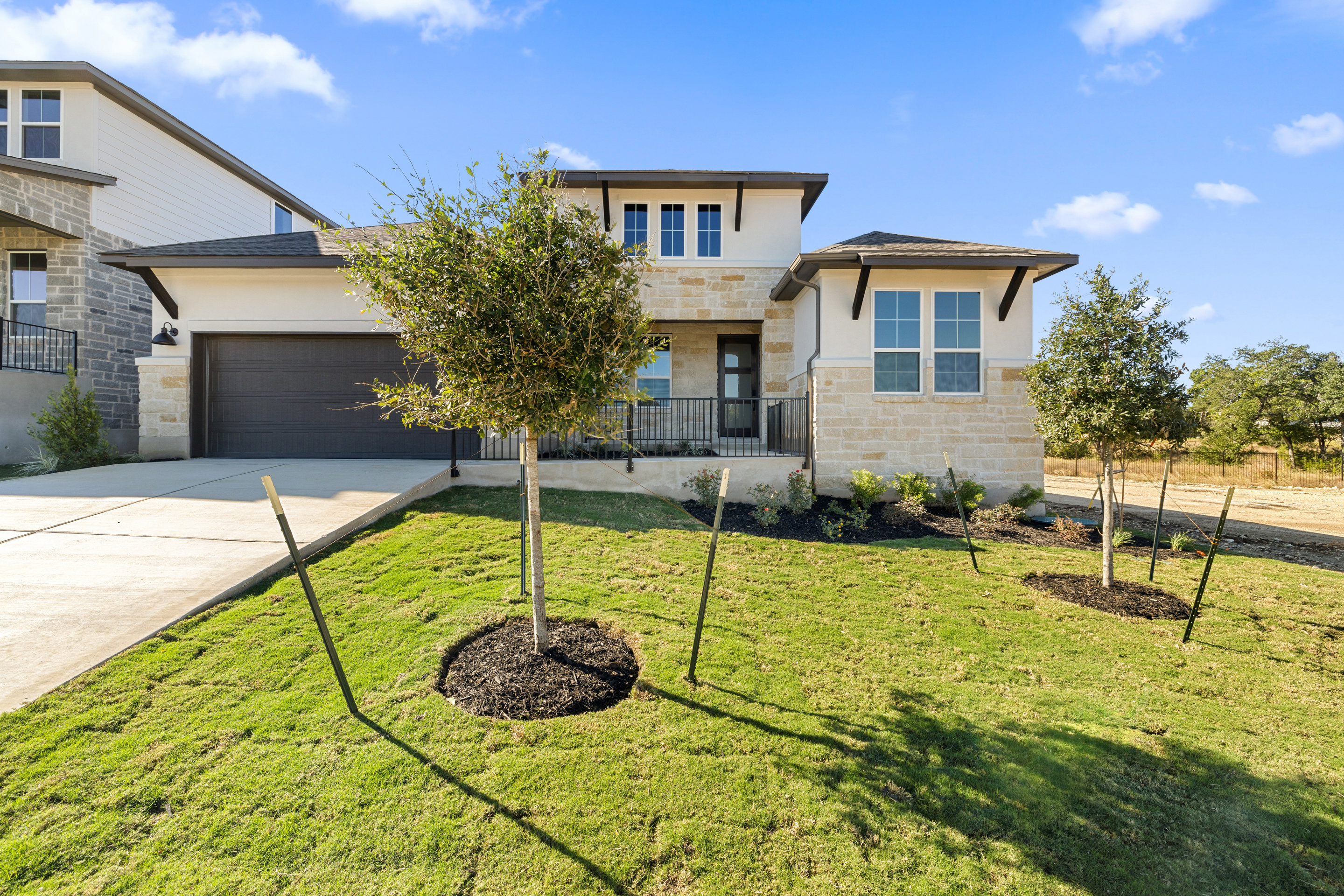 A modern two-story house with a well-manicured lawn, surrounded by trees and a clear blue sky with fluffy clouds.