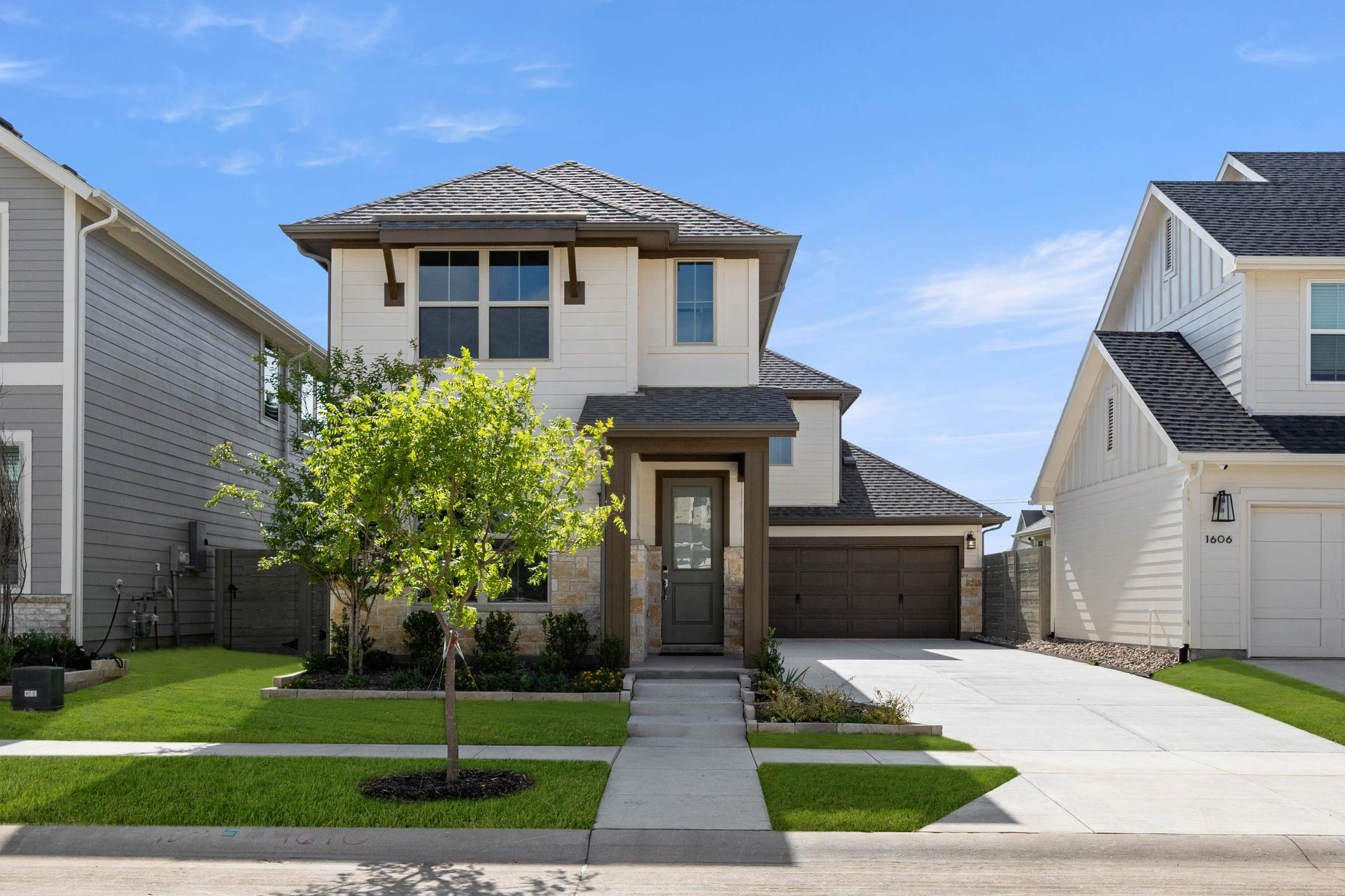 A two-story residential house with a well-manicured lawn, surrounded by other similar houses in a suburban neighborhood.