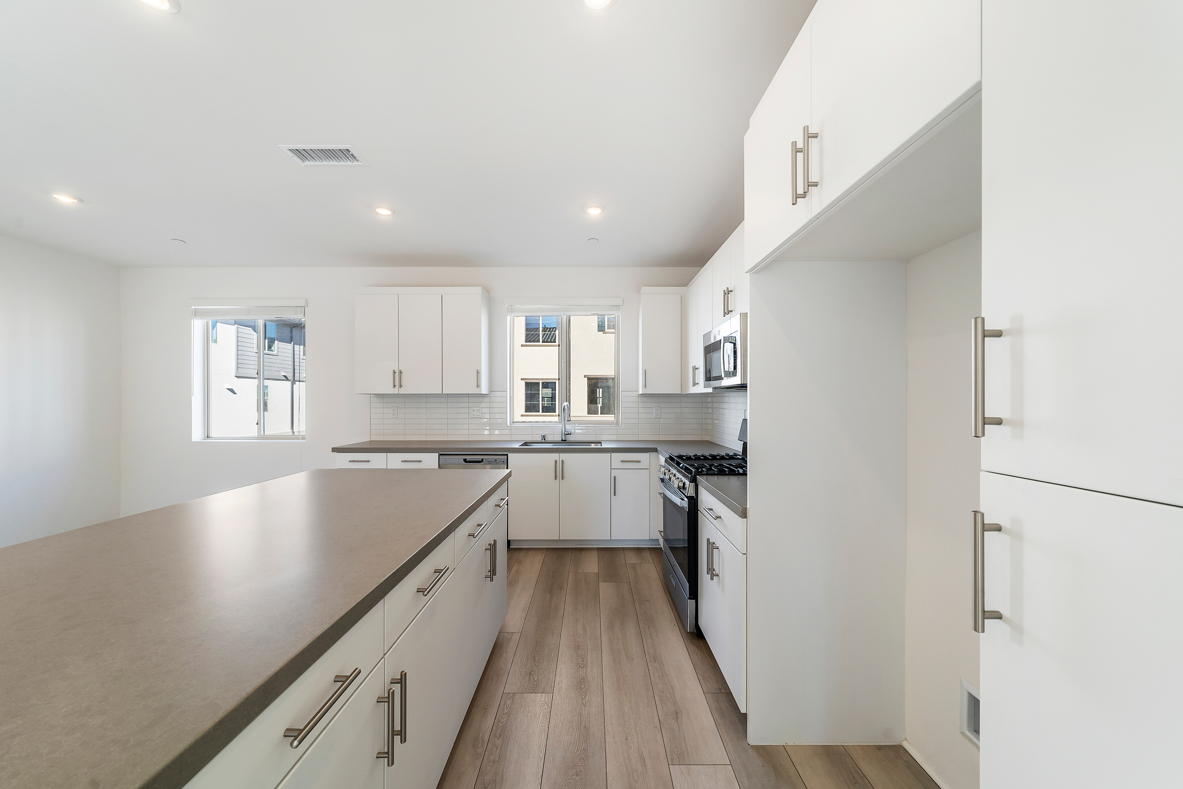 A modern, bright kitchen with white cabinets, stainless steel appliances, and a wooden floor.