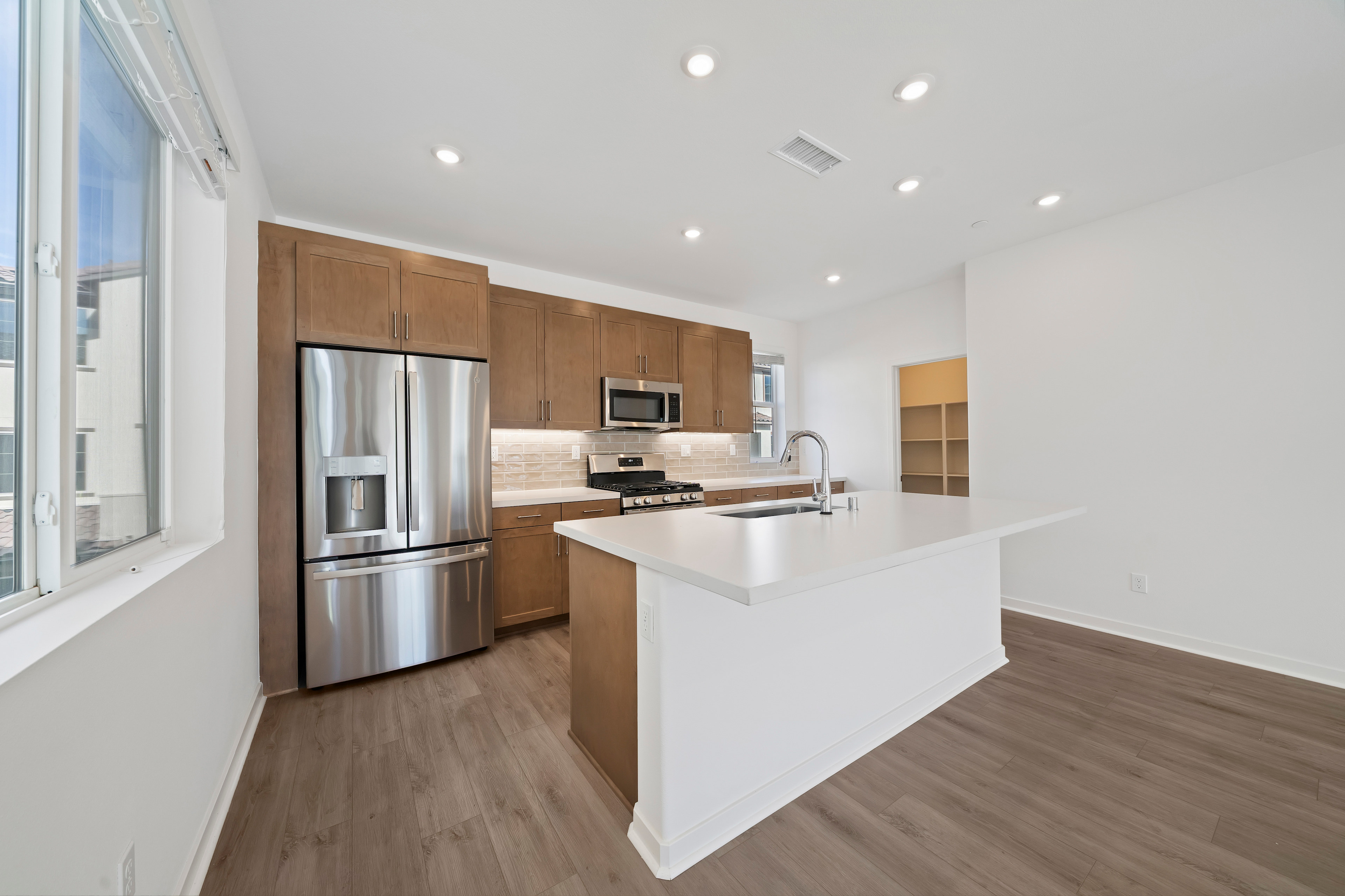 A modern, open-concept kitchen with stainless steel appliances, wooden cabinets, and a white countertop island, set against a bright, airy backdrop.