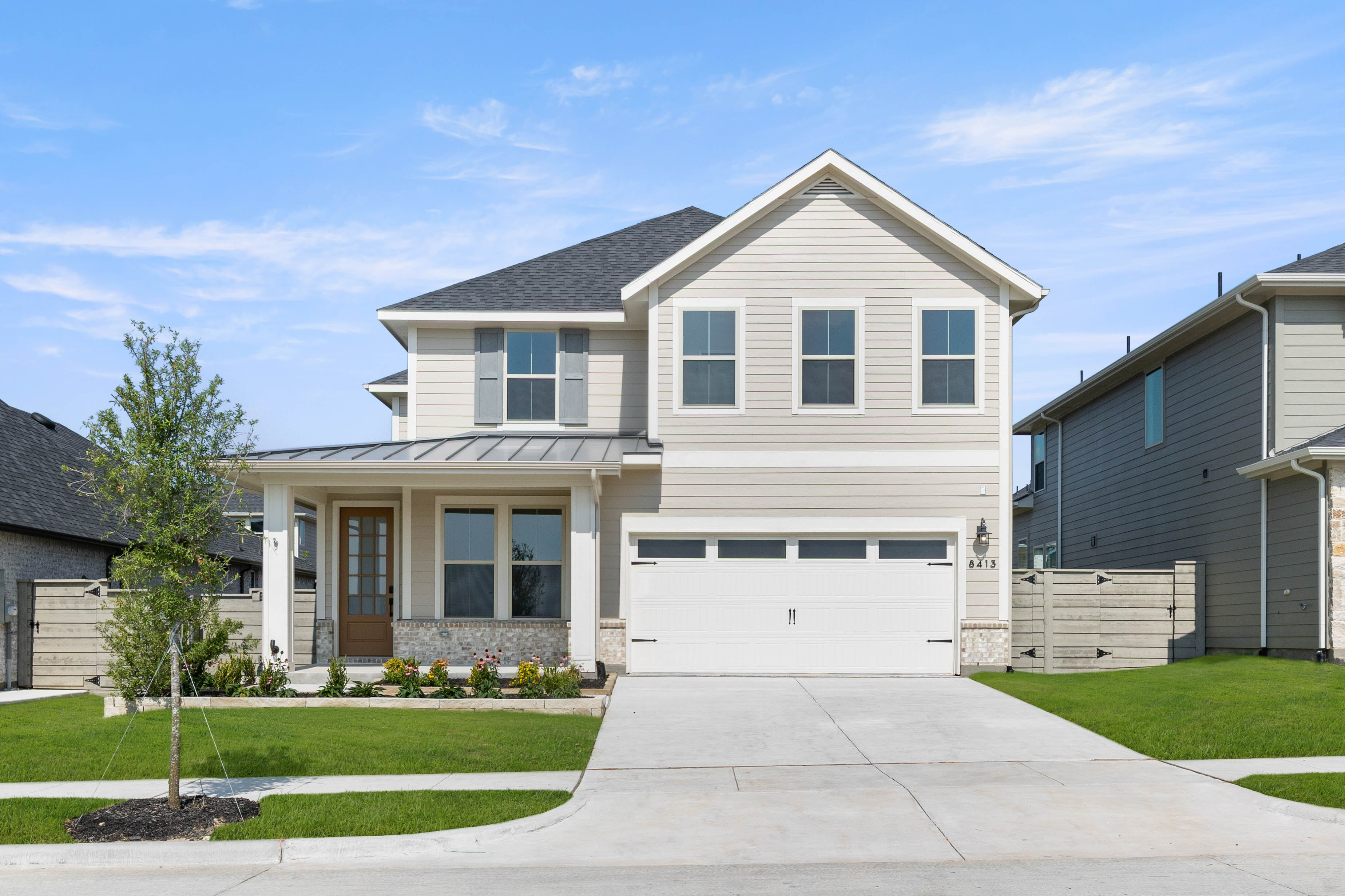 A two-story house with a white exterior, a gabled roof, and a well-manicured lawn in the foreground, set against a clear blue sky with some clouds.