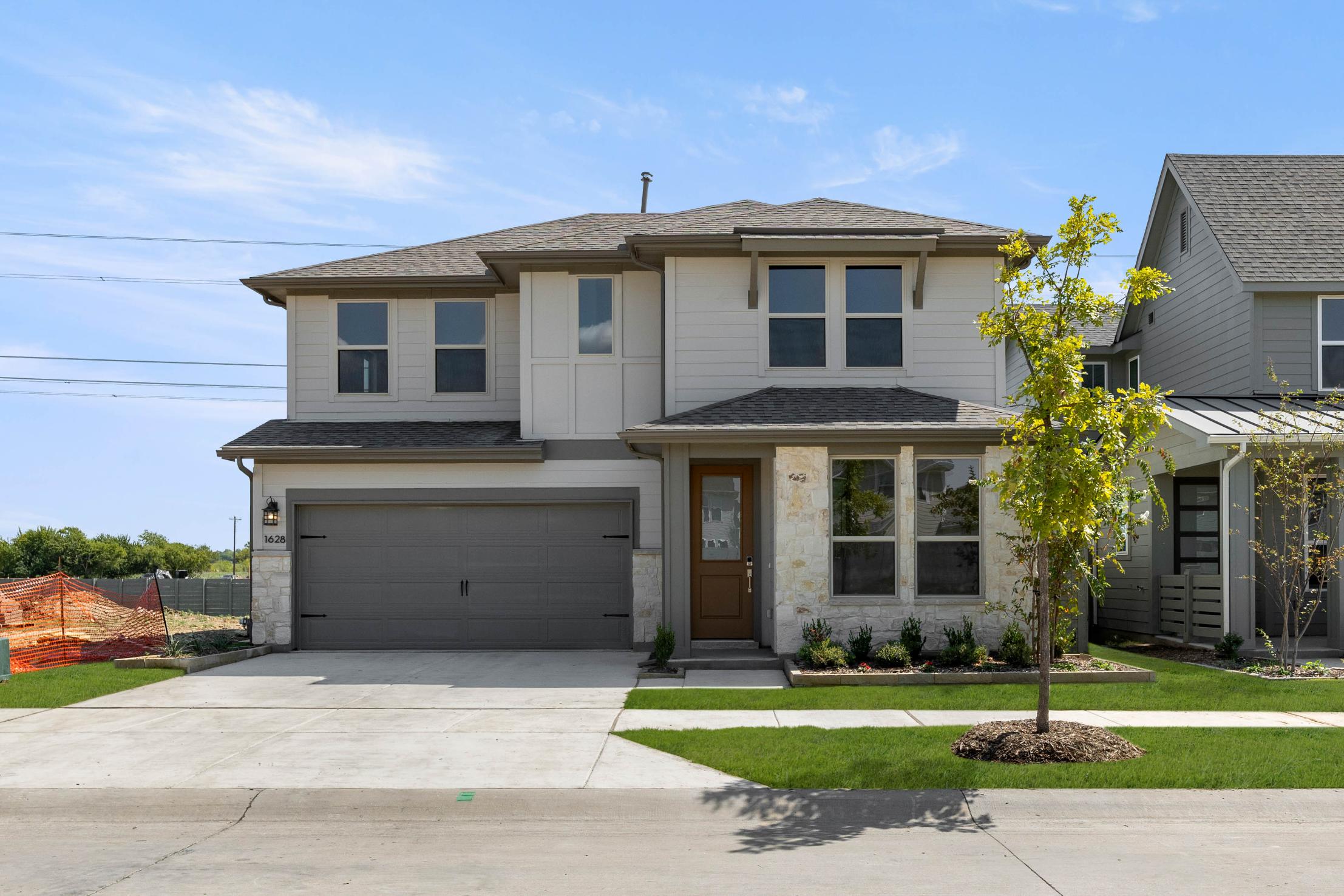 A two-story residential house with a garage, surrounded by a well-manicured lawn and landscaping, set against a clear blue sky with some clouds.