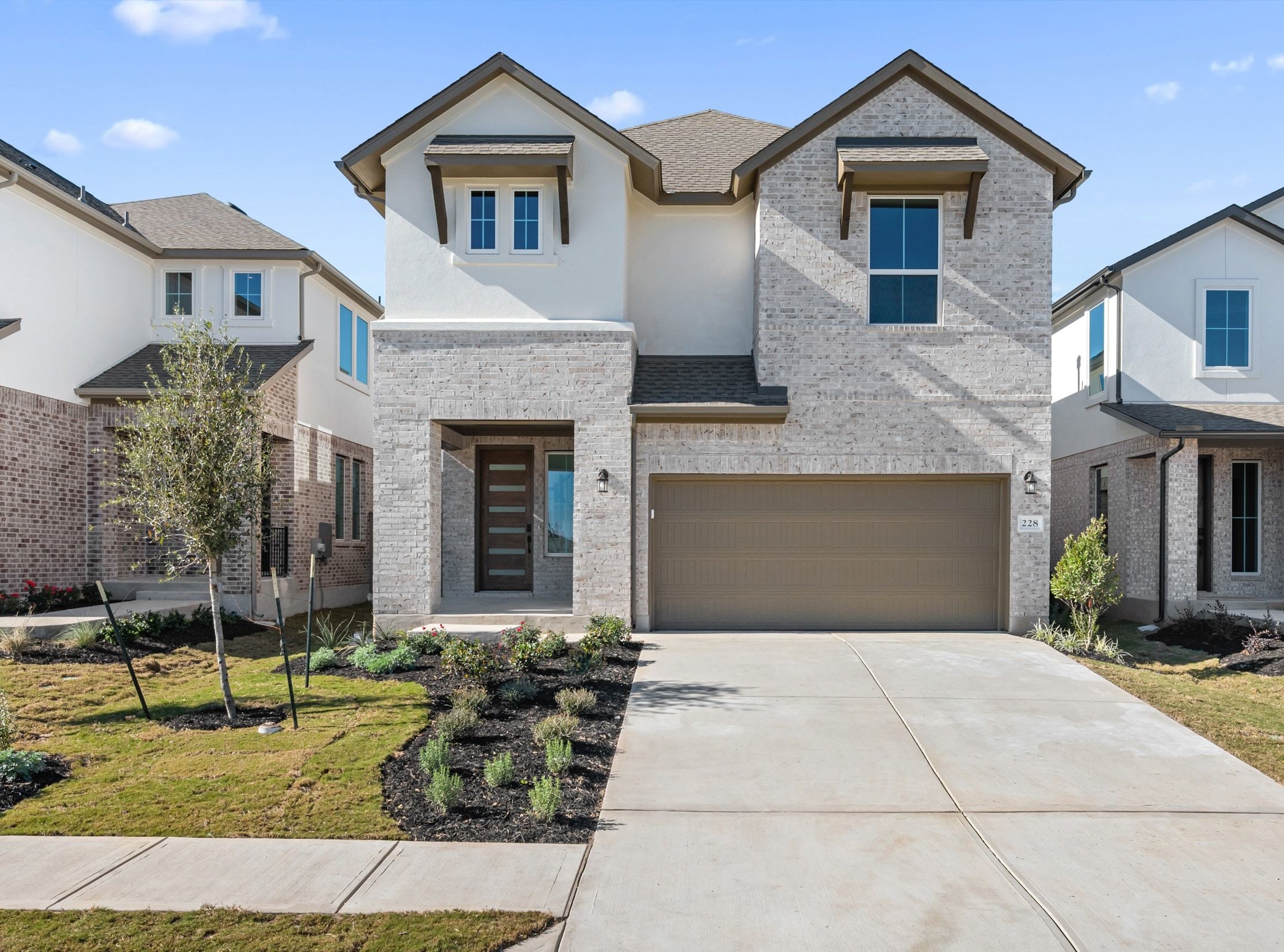 A two-story residential house with a garage, surrounded by a well-manicured lawn and landscaping, set against a backdrop of a clear sky with scattered clouds.