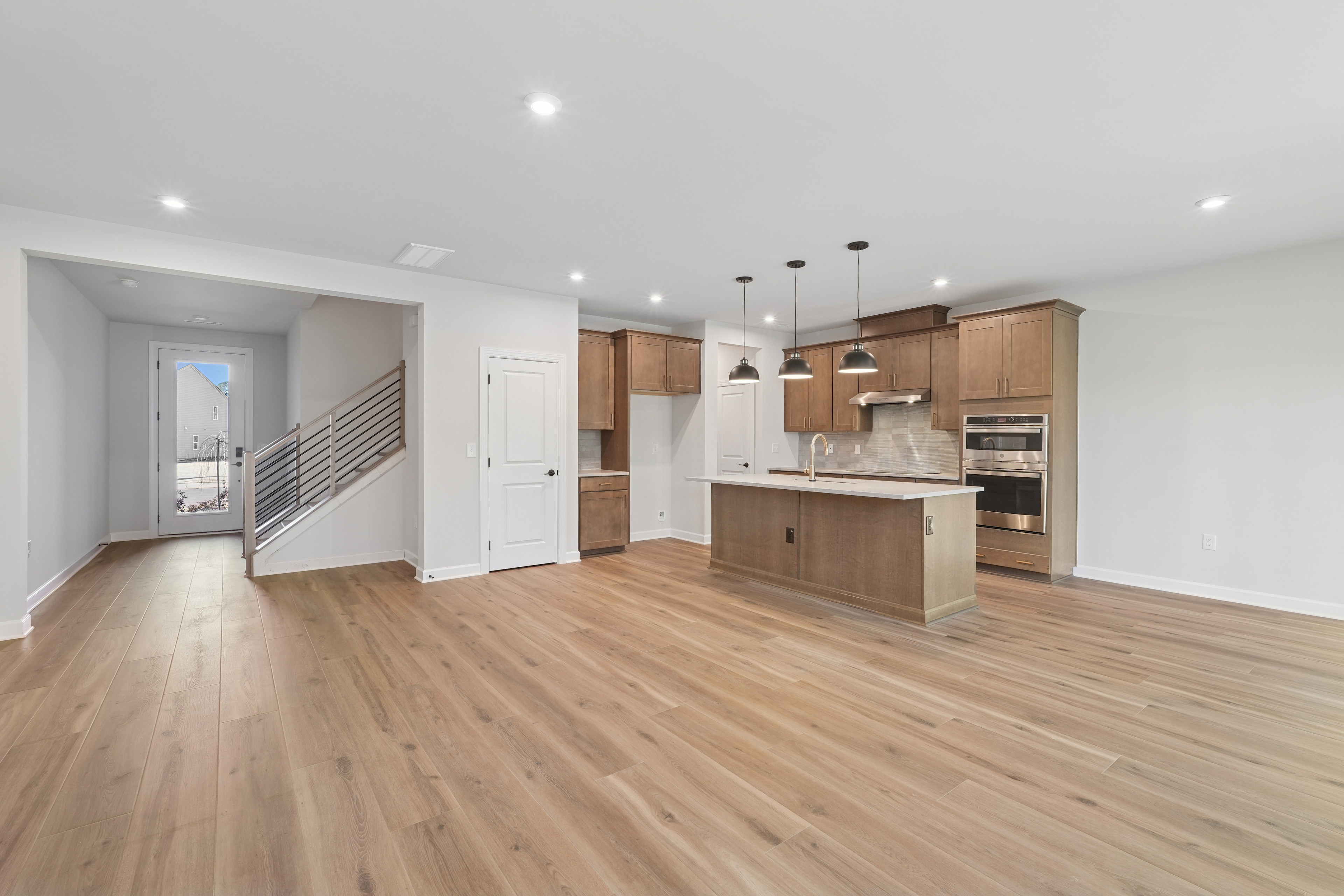 A modern, open-concept kitchen and living space with light-colored wood floors, white walls, and wooden cabinetry.