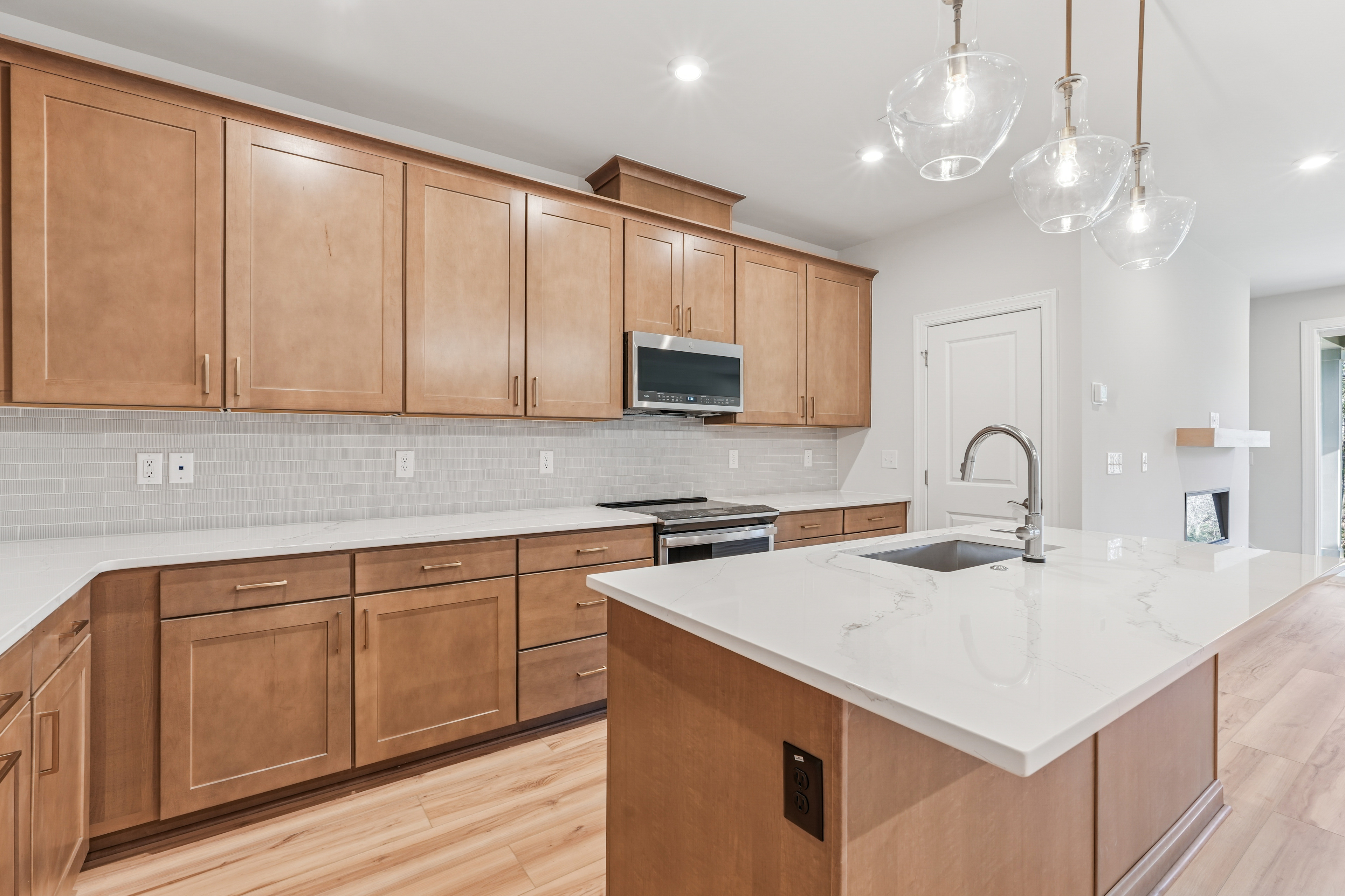 A modern, well-lit kitchen with light wood cabinetry, a white countertop, and pendant lighting fixtures.