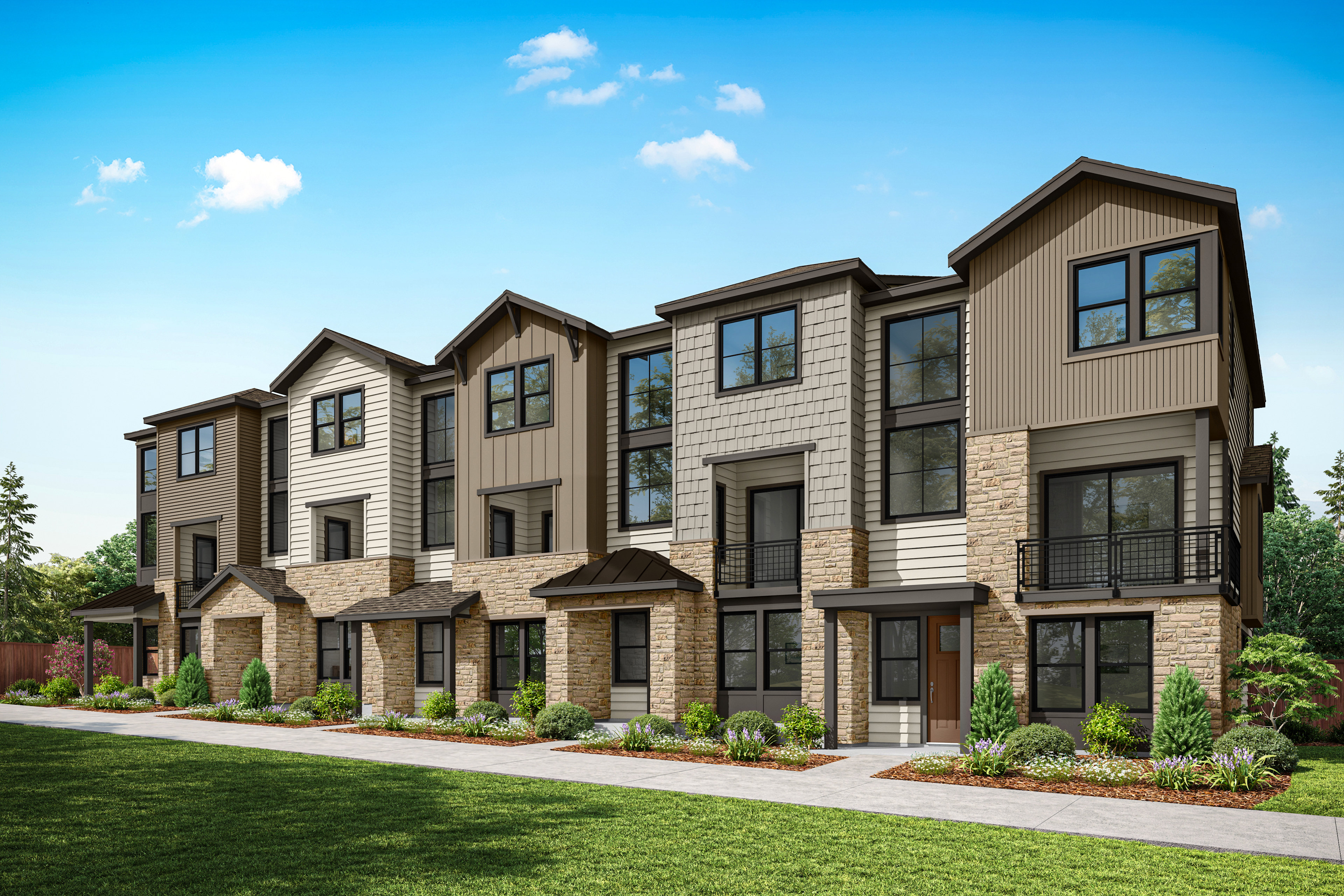 A row of modern, multi-story townhouses with stone and siding exteriors, surrounded by a well-manicured lawn and landscaping, set against a clear blue sky with fluffy white clouds.