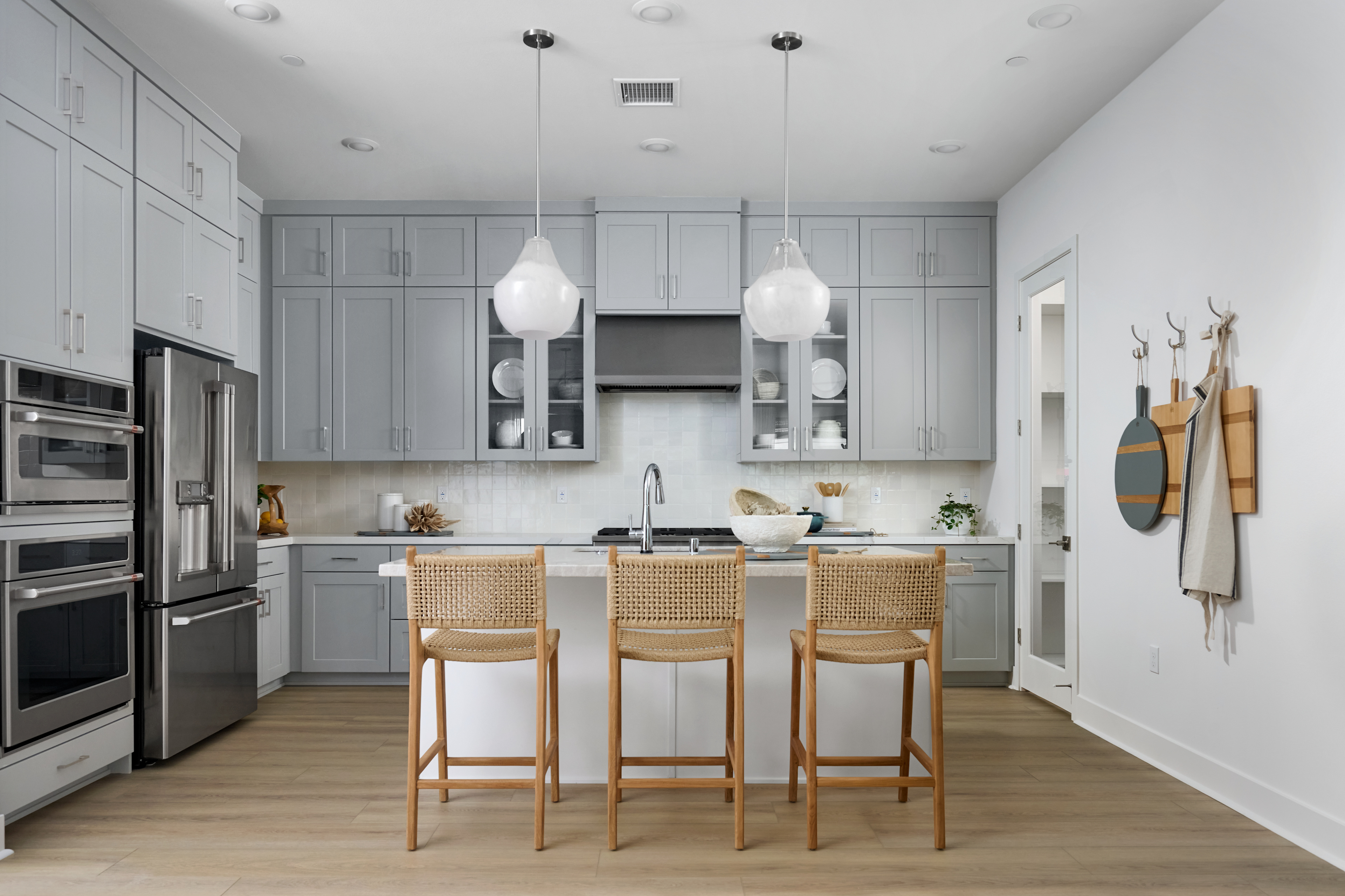 A modern, well-appointed kitchen with gray cabinets, stainless steel appliances, and woven bar stools at a central island.