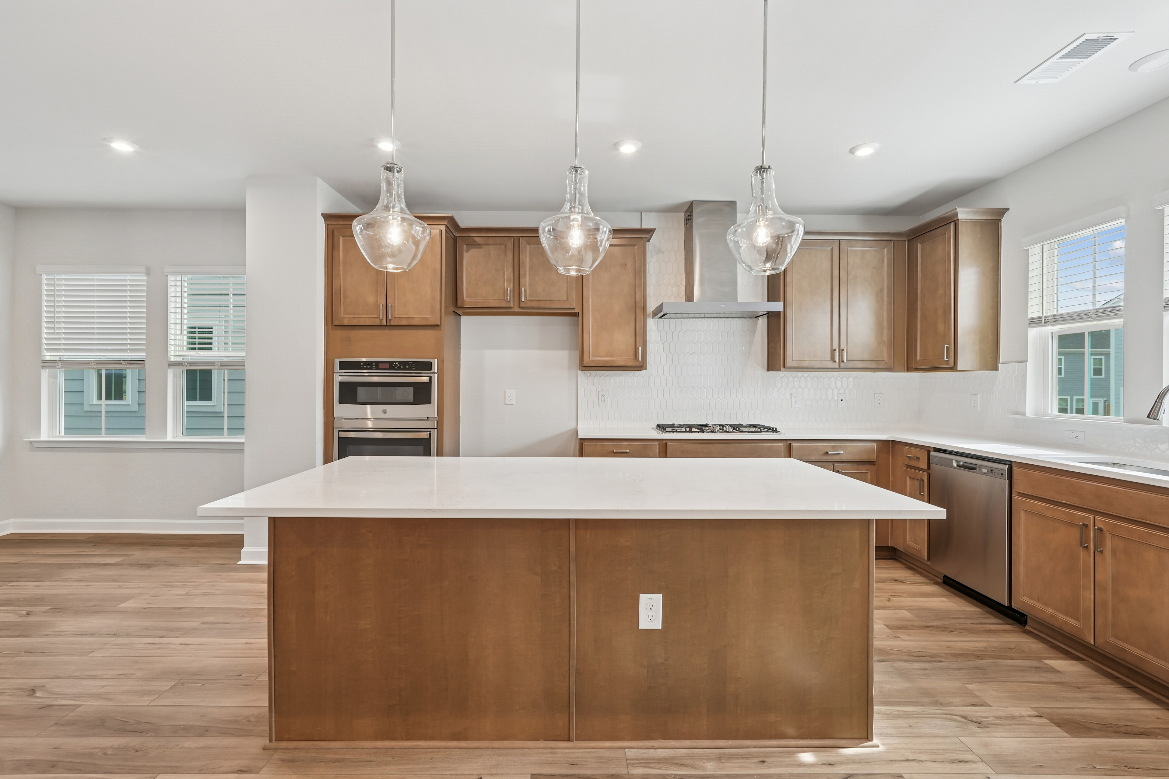 A modern, open-concept kitchen with wooden cabinets, a large island, and pendant lighting fixtures hanging above the counter.