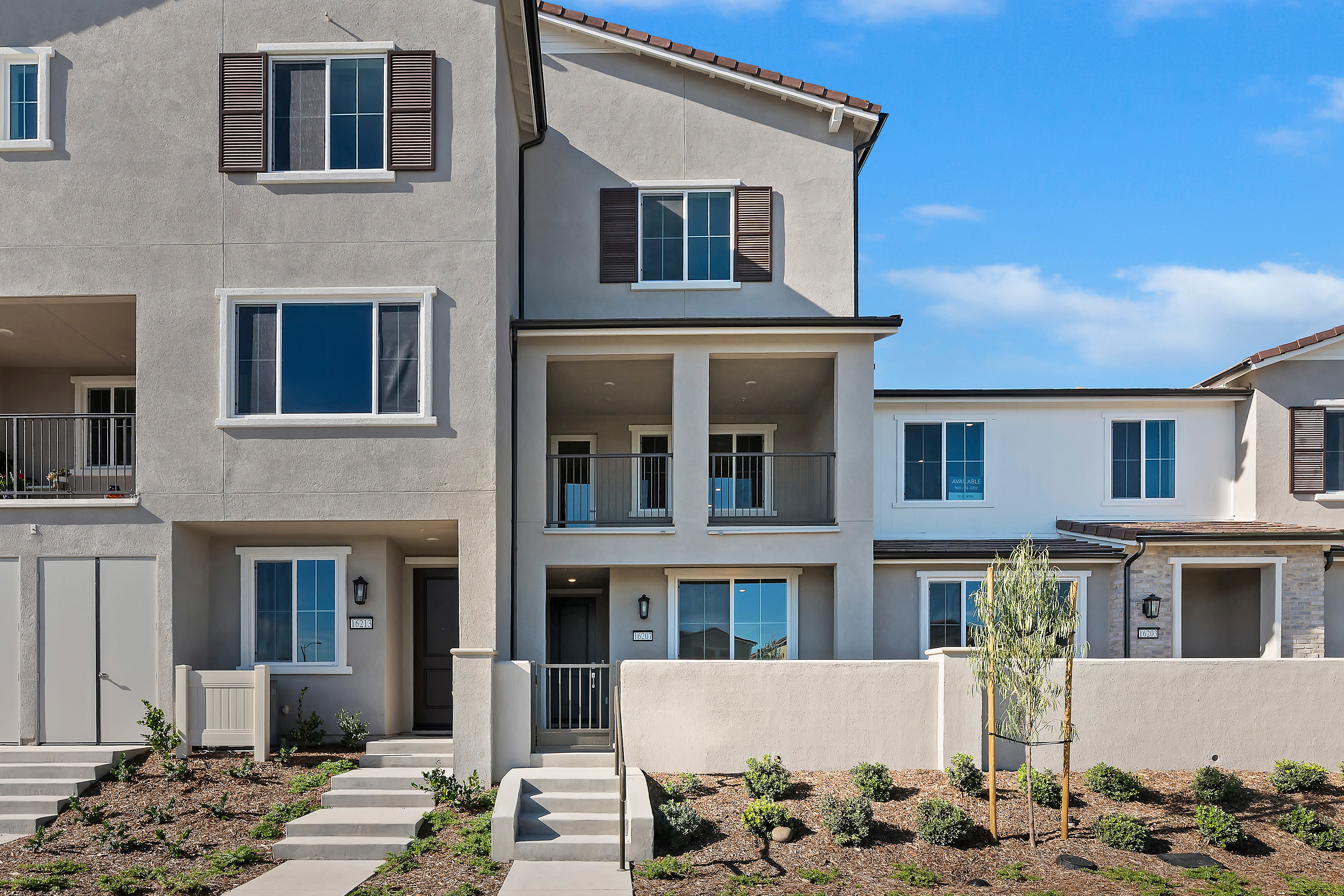 A modern, multi-story townhouse with a landscaped front yard and a clear blue sky in the background.