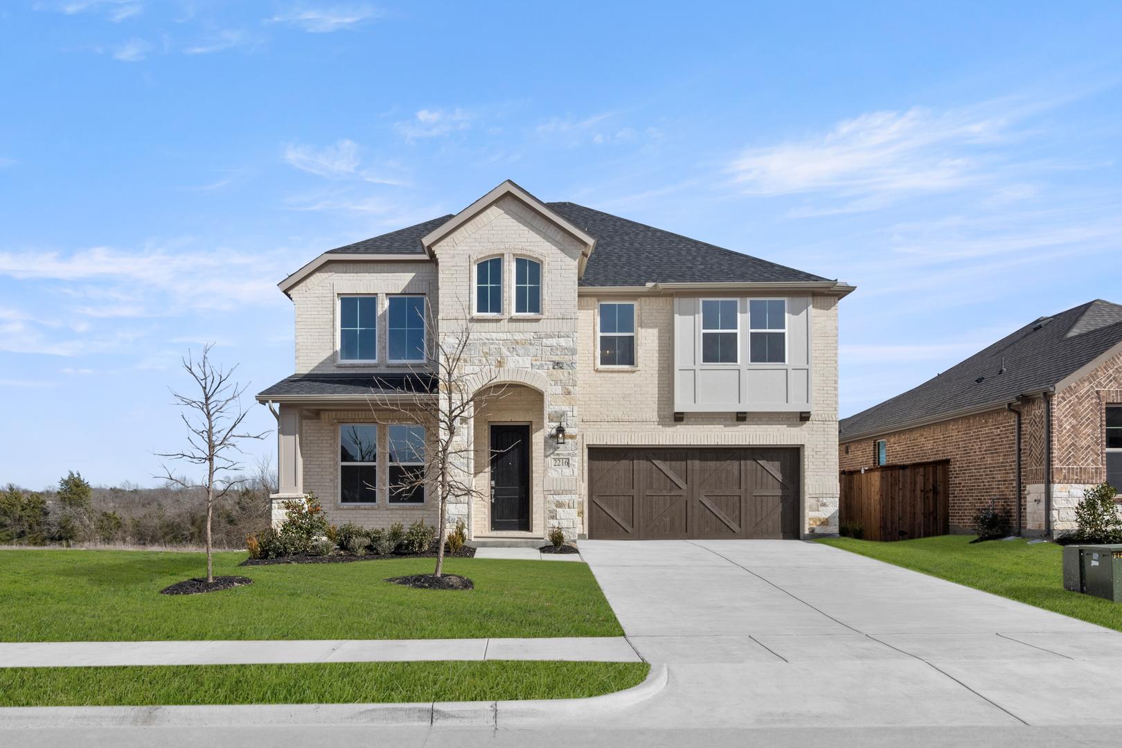 A two-story house with a stone exterior, a garage, and a well-manicured lawn set against a blue sky with scattered clouds.