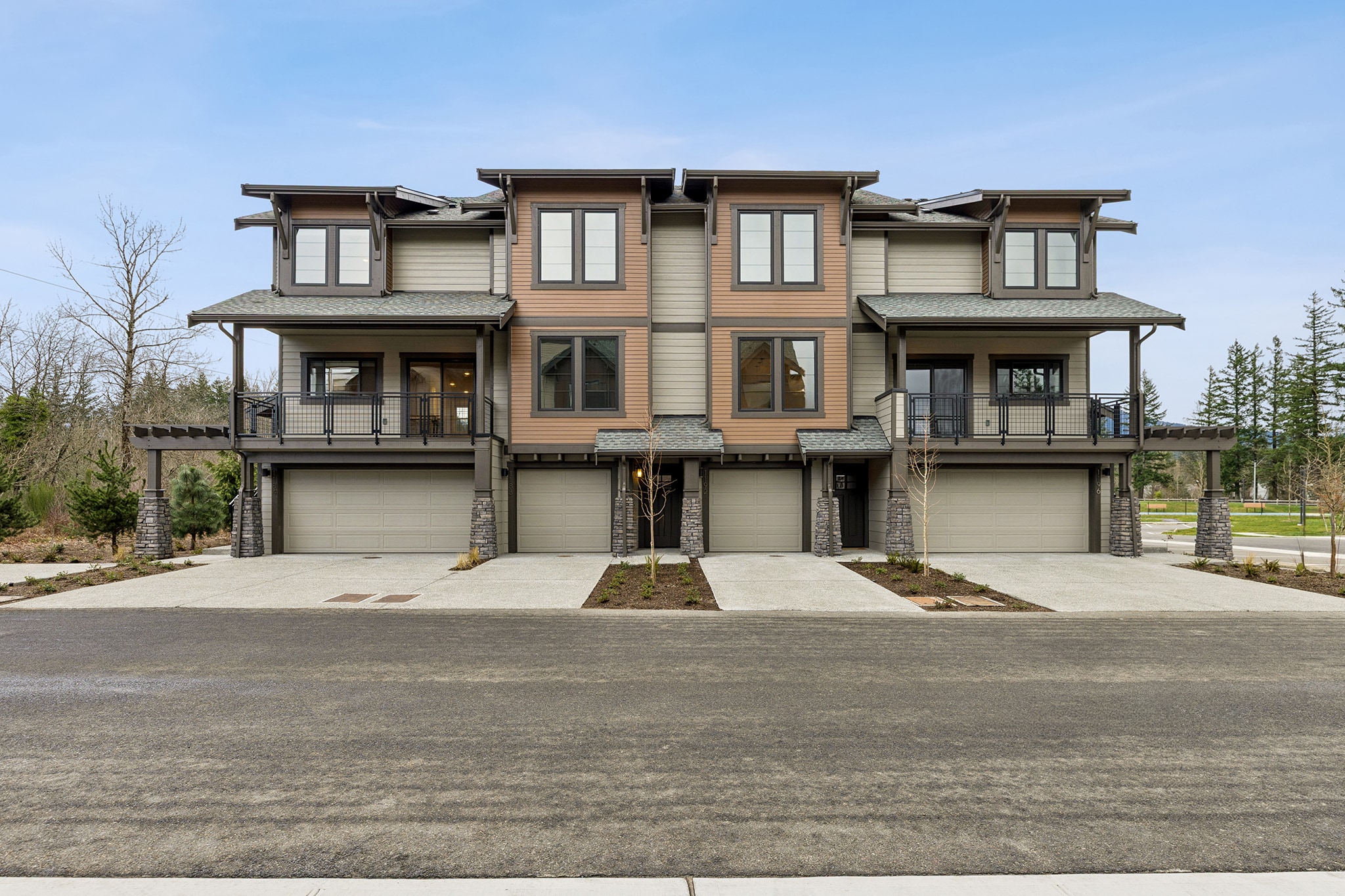 A multi-unit residential building with a modern, rustic-style architecture, surrounded by a paved driveway and a grassy area in the background.