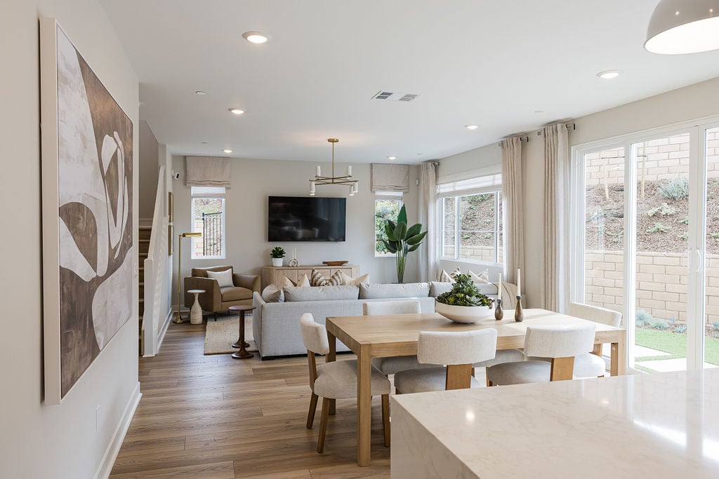 A modern and cozy living room with a dining area, featuring neutral tones, natural wood accents, and large windows that let in ample natural light.