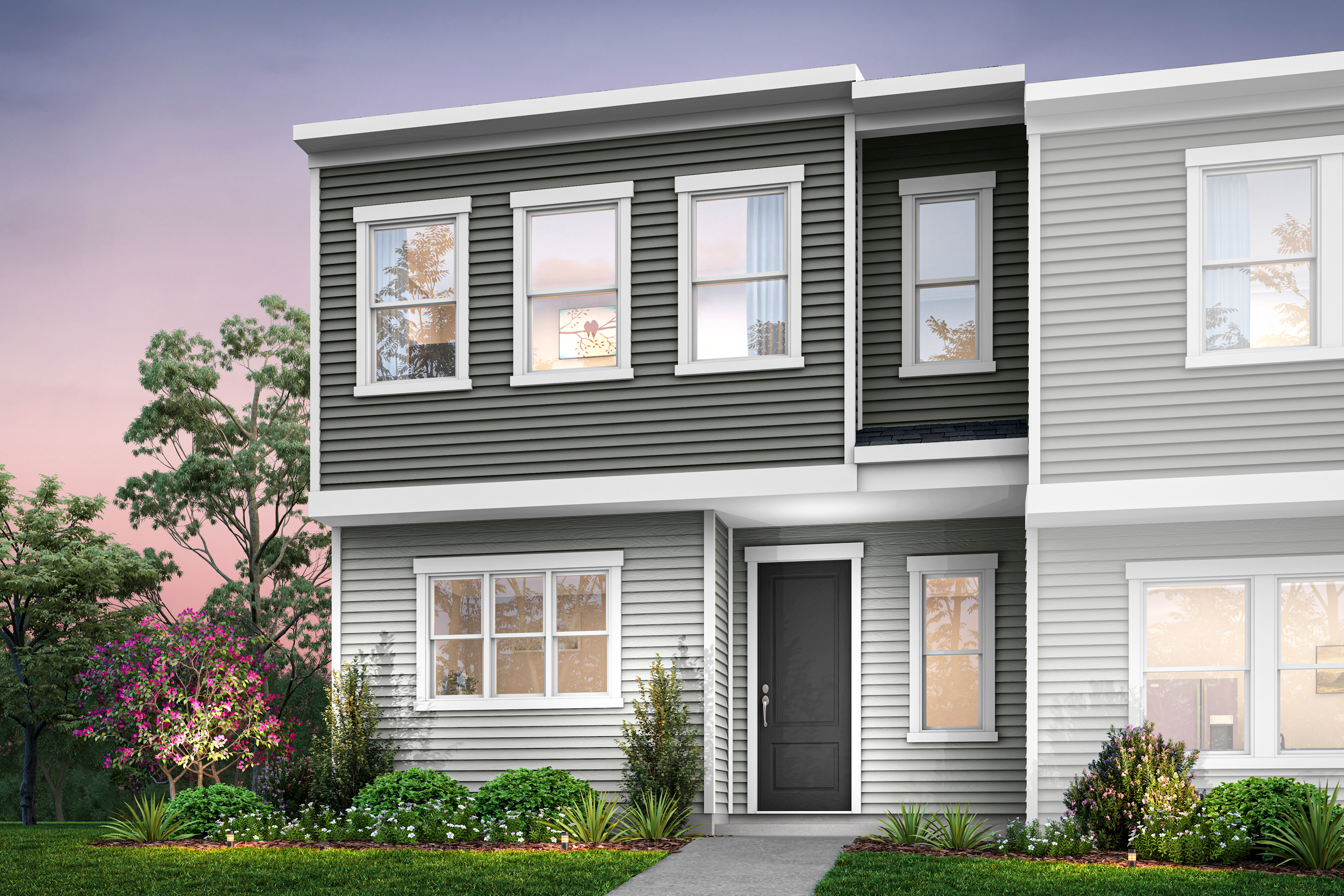 A modern two-story townhouse with gray siding, surrounded by lush greenery and a well-manicured lawn in the foreground.