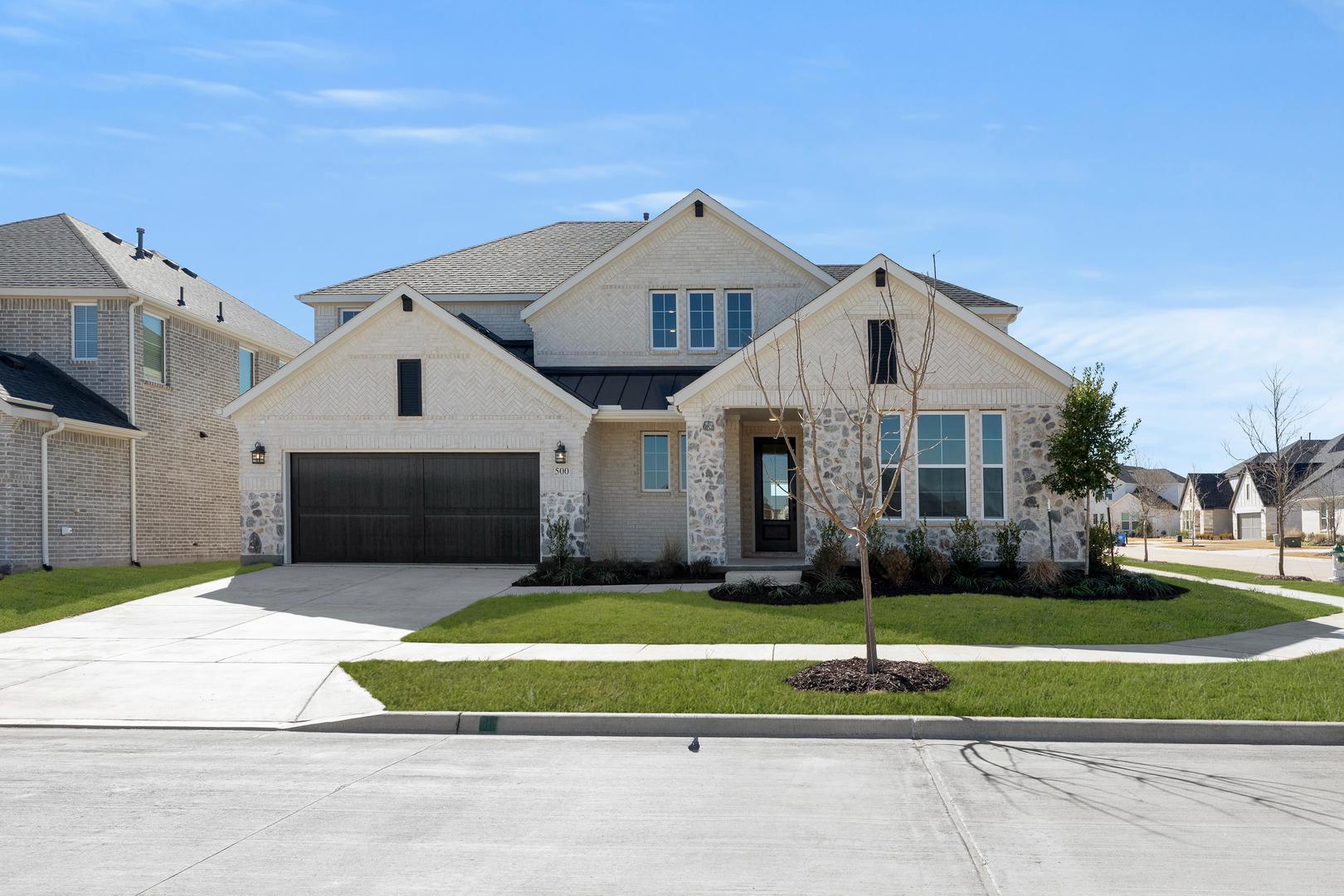 A large, two-story house with a gabled roof, a garage, and a well-manicured lawn in the foreground, set against a clear blue sky in the background.
