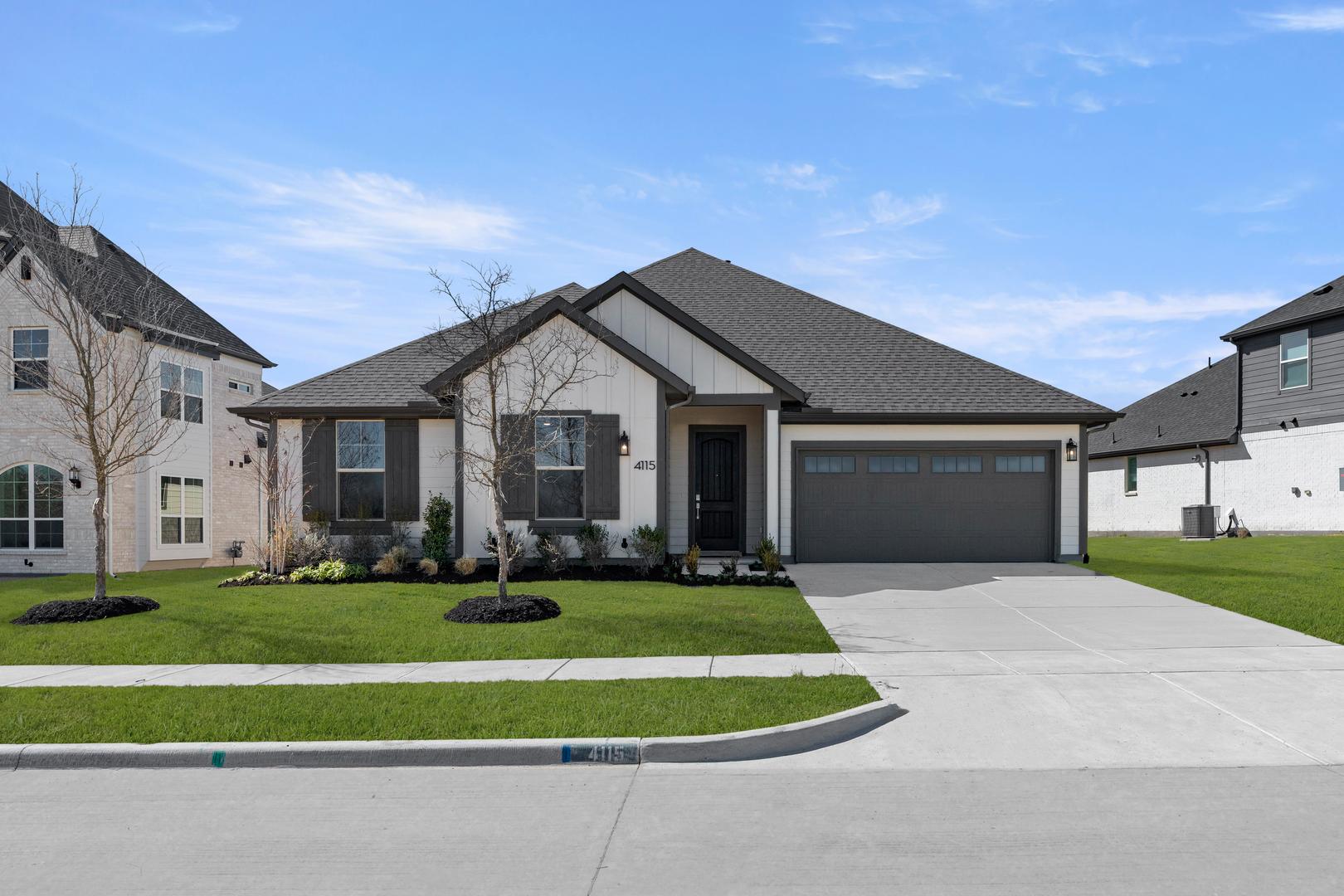 A modern two-story house with a gray exterior, a gabled roof, and a well-manicured lawn in the foreground, set against a clear blue sky.