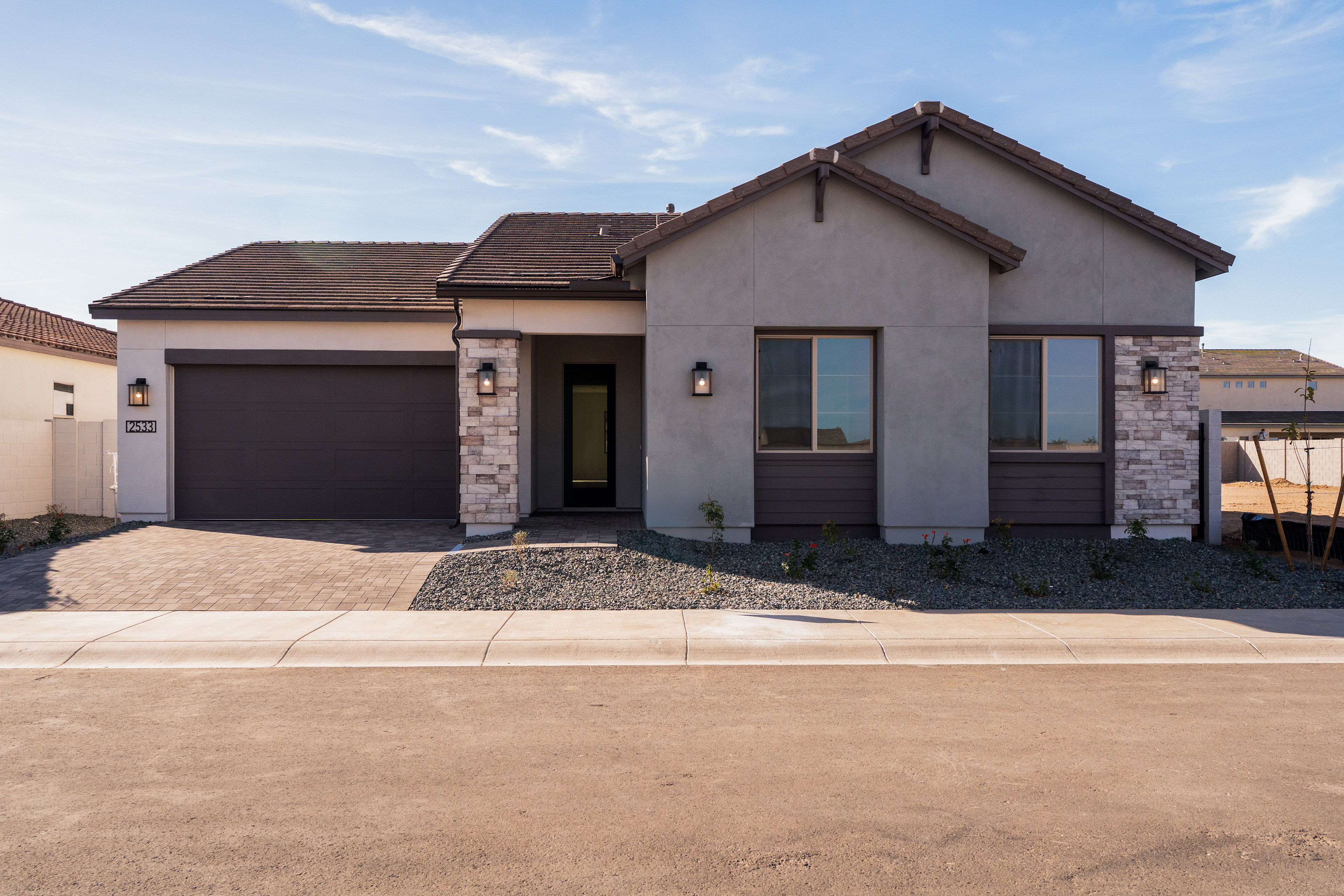 A single-story residential house with a garage, featuring a stucco exterior and stone accents, set against a clear blue sky with wispy clouds.