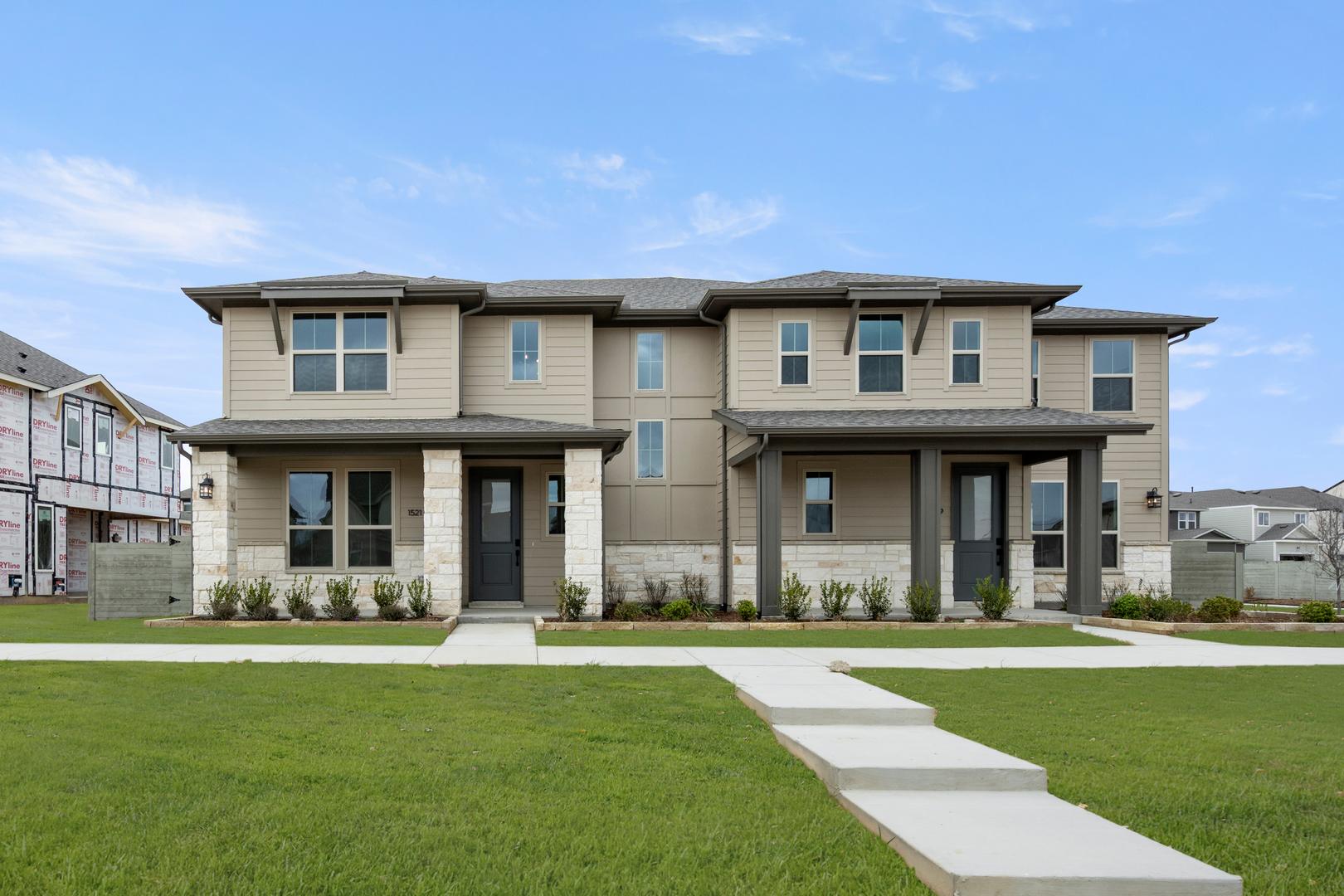 A modern, two-story townhouse complex with a well-manicured lawn and a paved walkway leading to the front entrances.