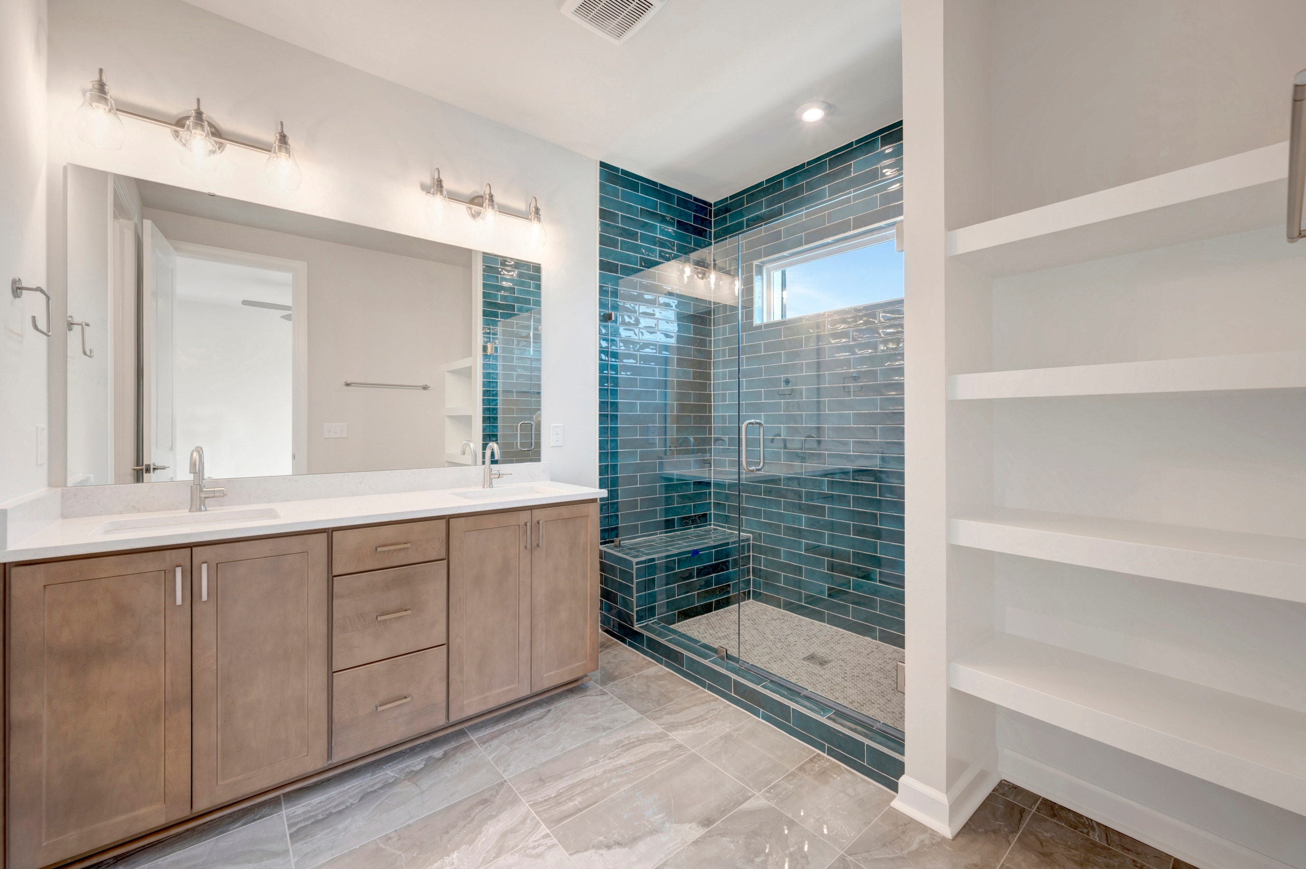 A modern bathroom with a wooden vanity, a large mirror, and a tiled shower enclosure with a glass door, set against a neutral color palette.