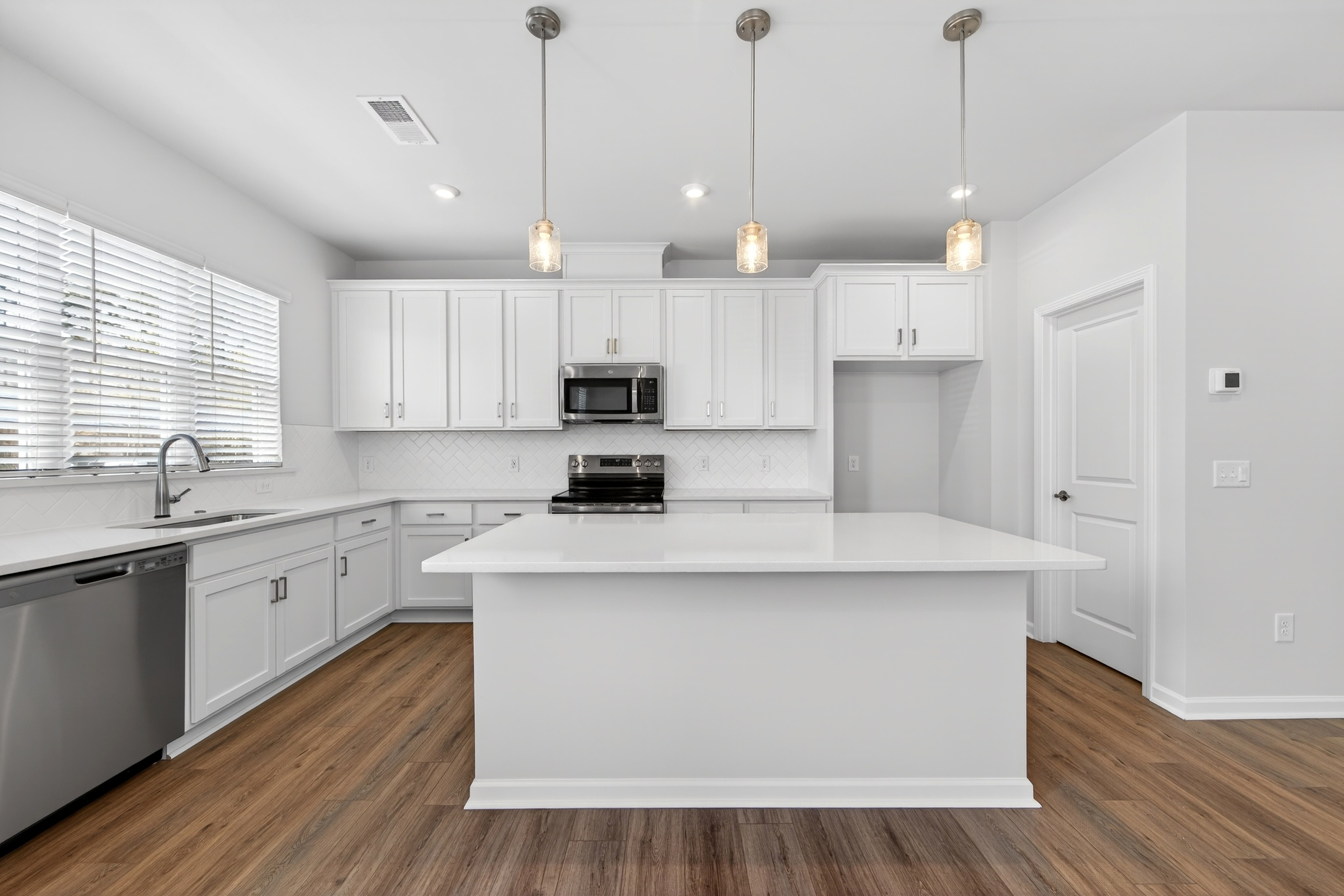 A modern, bright, and spacious kitchen with white cabinets, a central island, and hardwood floors.