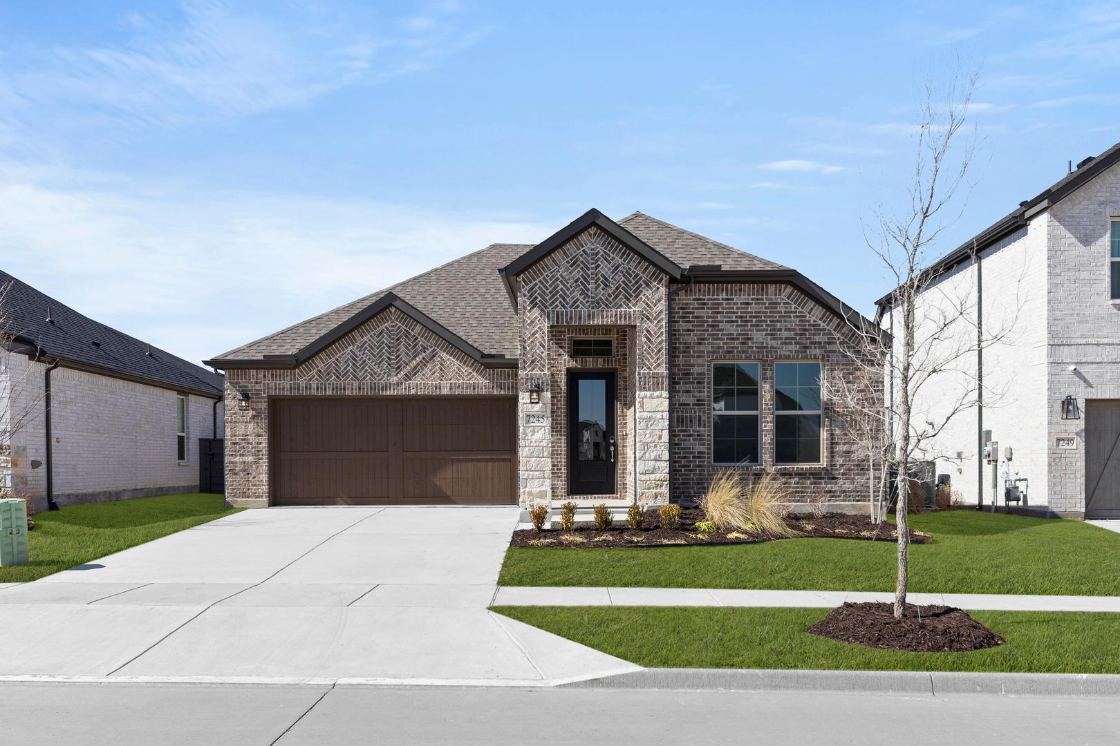 A two-story brick house with a gabled roof, surrounded by a well-manicured lawn and a concrete driveway leading to a garage door.