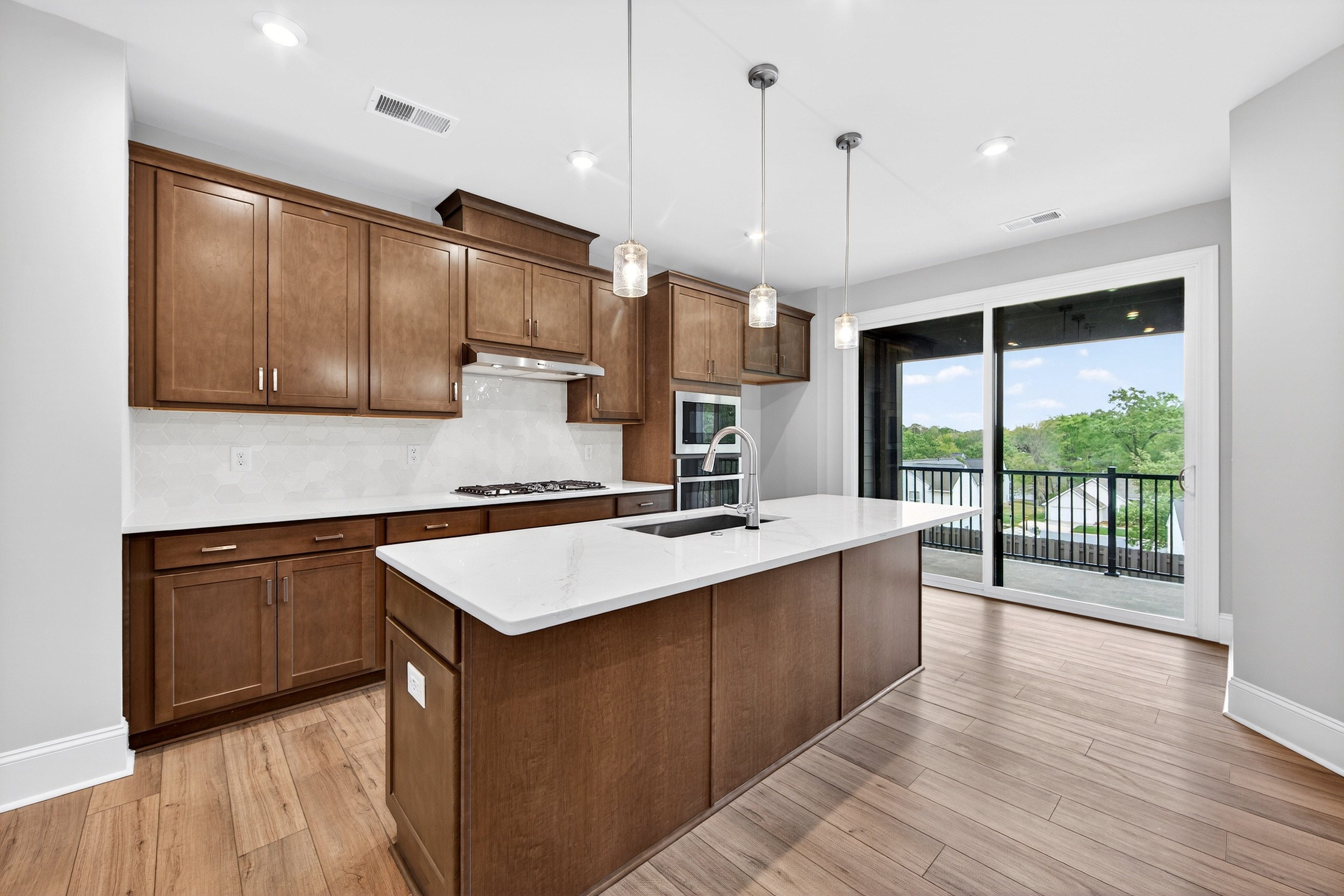 A modern kitchen with wooden cabinets, a white countertop, and a sliding glass door leading to a balcony or patio with a view of the outdoors.