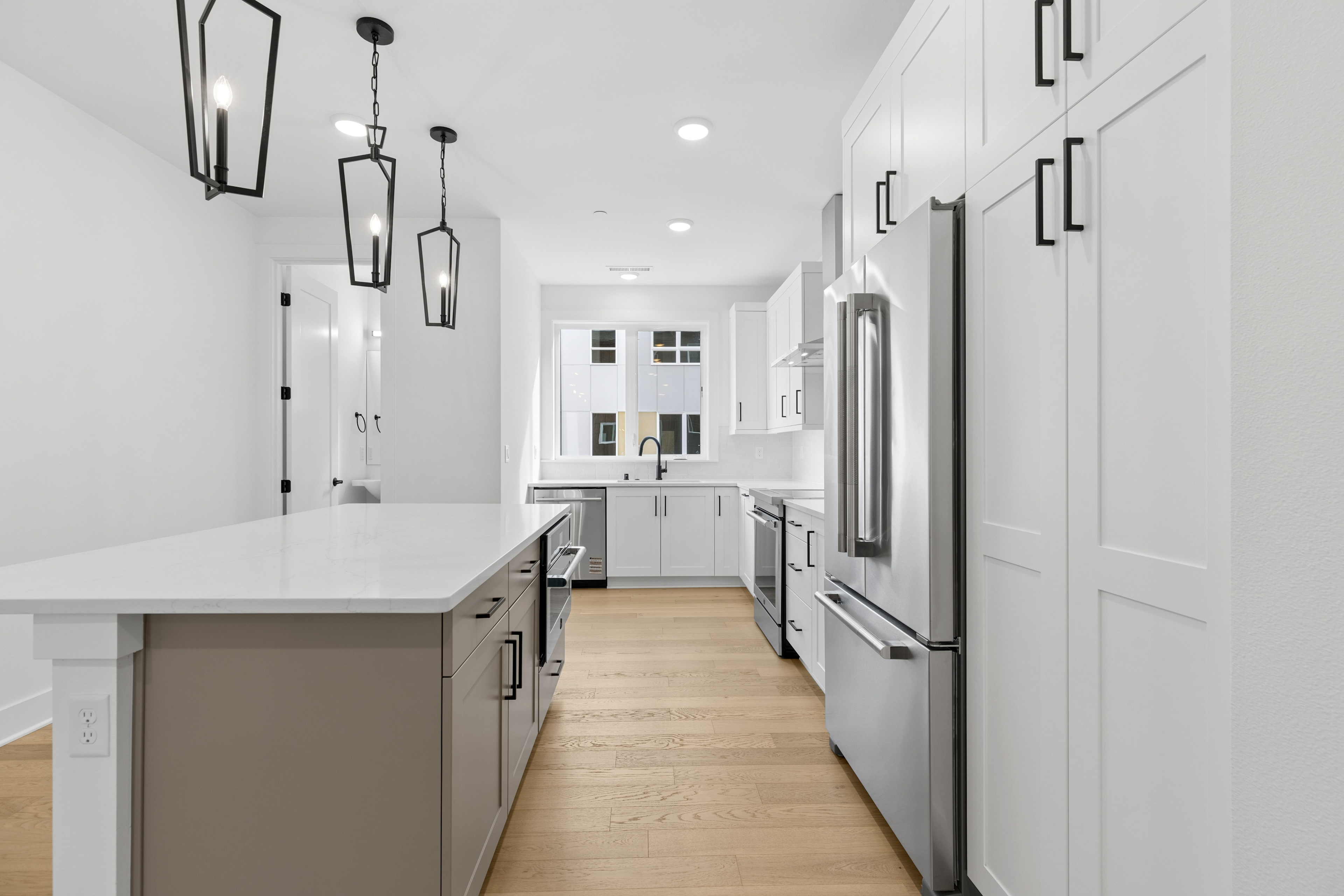 A modern, minimalist kitchen with white walls, gray cabinets, stainless steel appliances, and pendant lighting fixtures creating a sleek and stylish atmosphere.