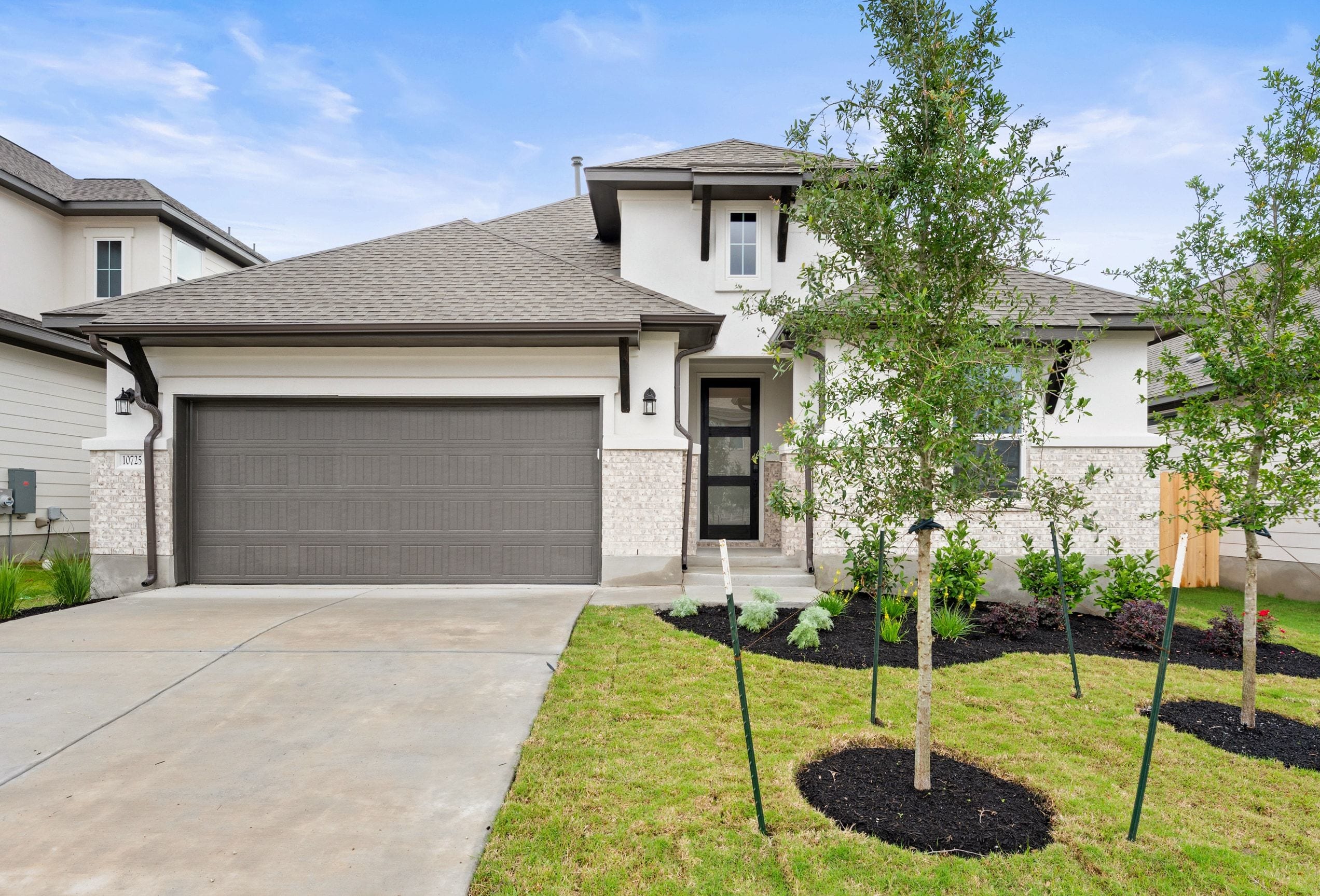 A modern two-story house with a gray exterior, a garage, and a well-manicured lawn with newly planted trees in the foreground.