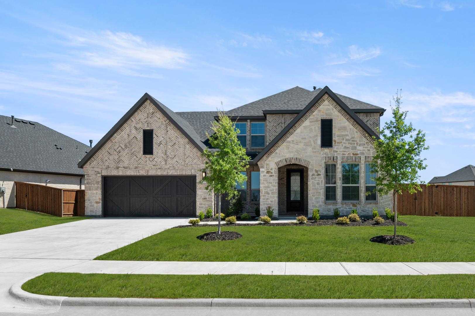 A large, two-story brick house with a gabled roof and a well-manicured lawn in the foreground, set against a clear blue sky with scattered clouds.