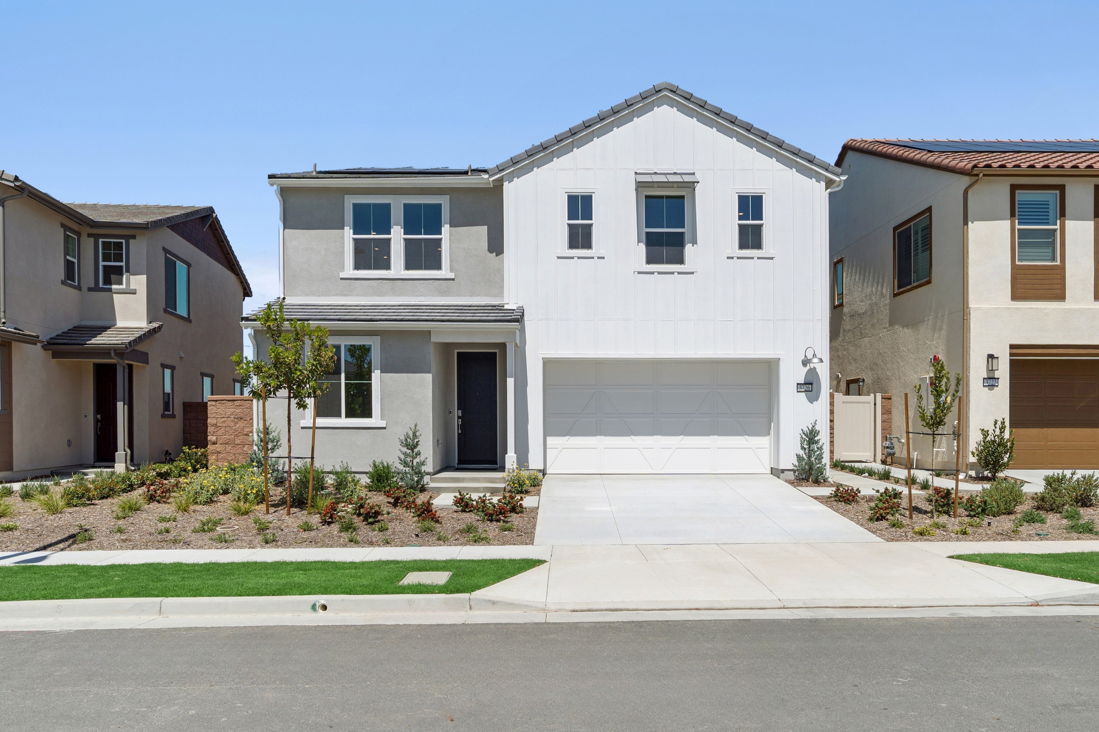 A modern two-story house with a white exterior, a garage, and a well-manicured lawn in the foreground, set against a clear blue sky.