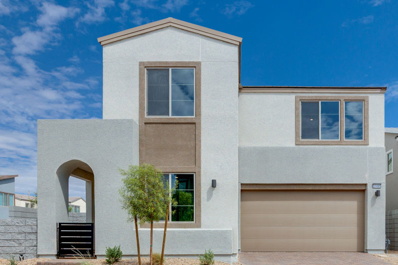 A modern, two-story white and beige house with a garage door, surrounded by a clear blue sky and a few small trees in the foreground.