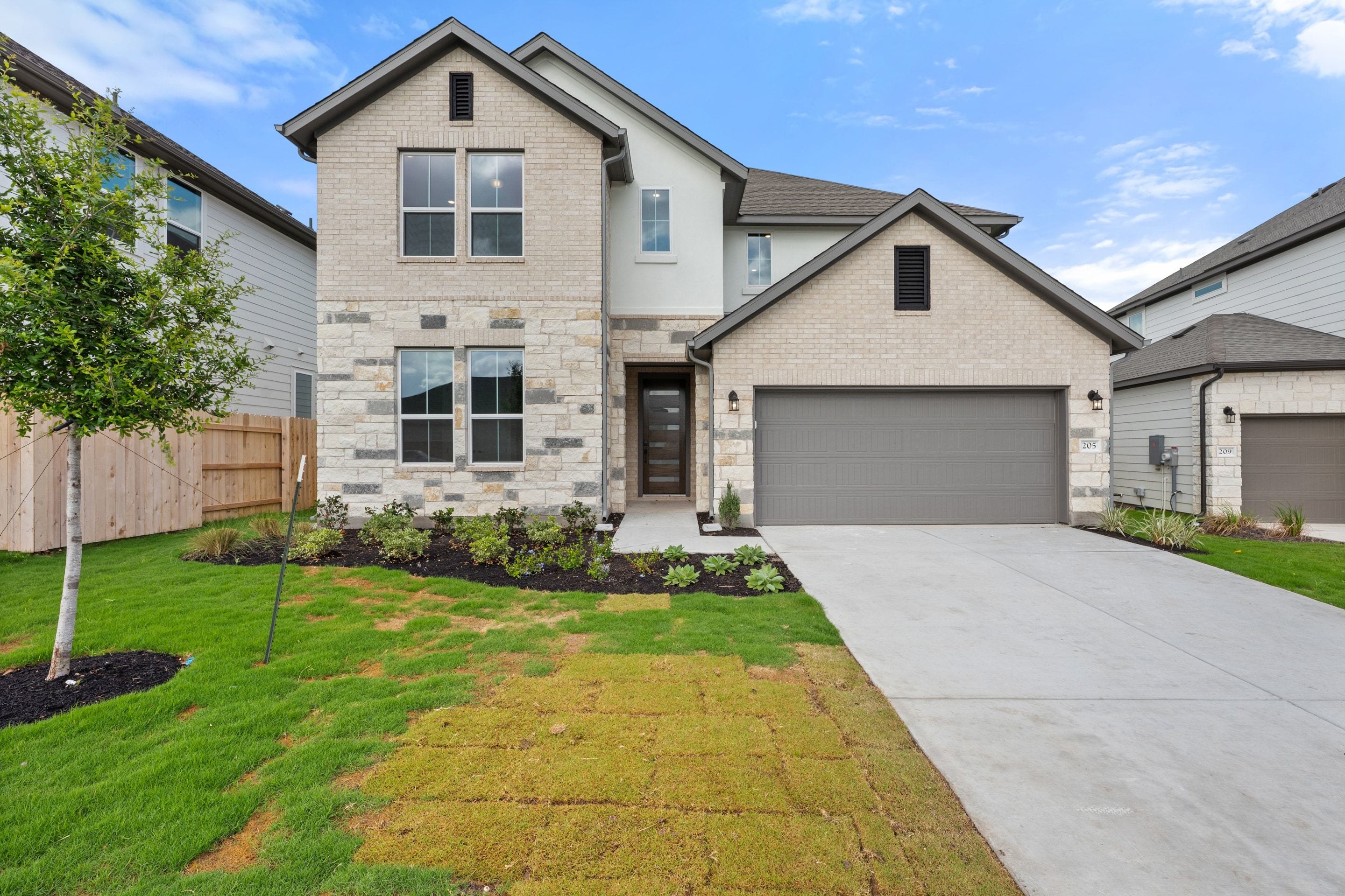 A two-story residential house with a gray exterior, a garage, and a well-manicured lawn in the foreground, set against a clear blue sky in the background.