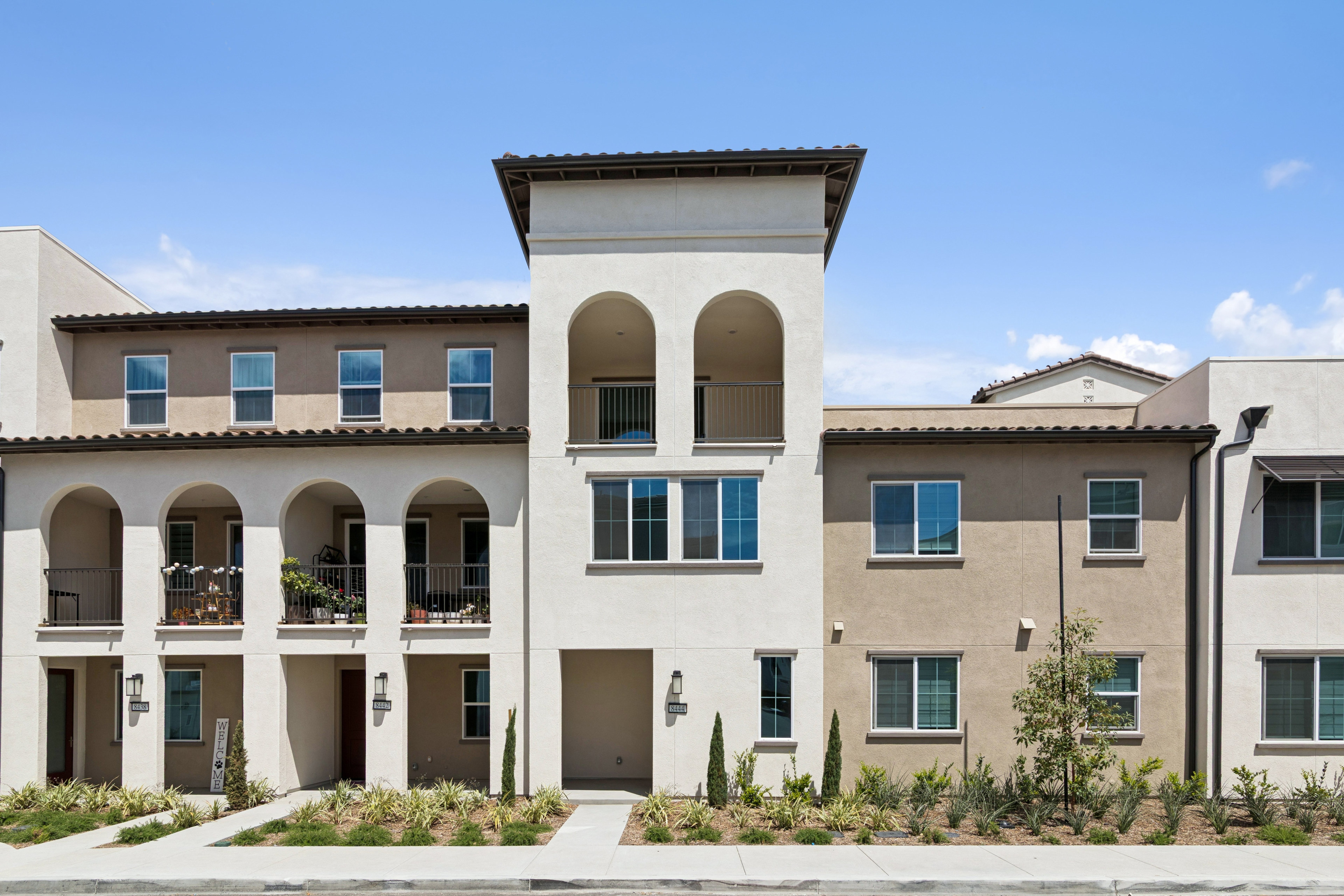 A multi-story residential building with a Mediterranean-style architecture, featuring arched windows, balconies, and a central tower, set against a clear blue sky.